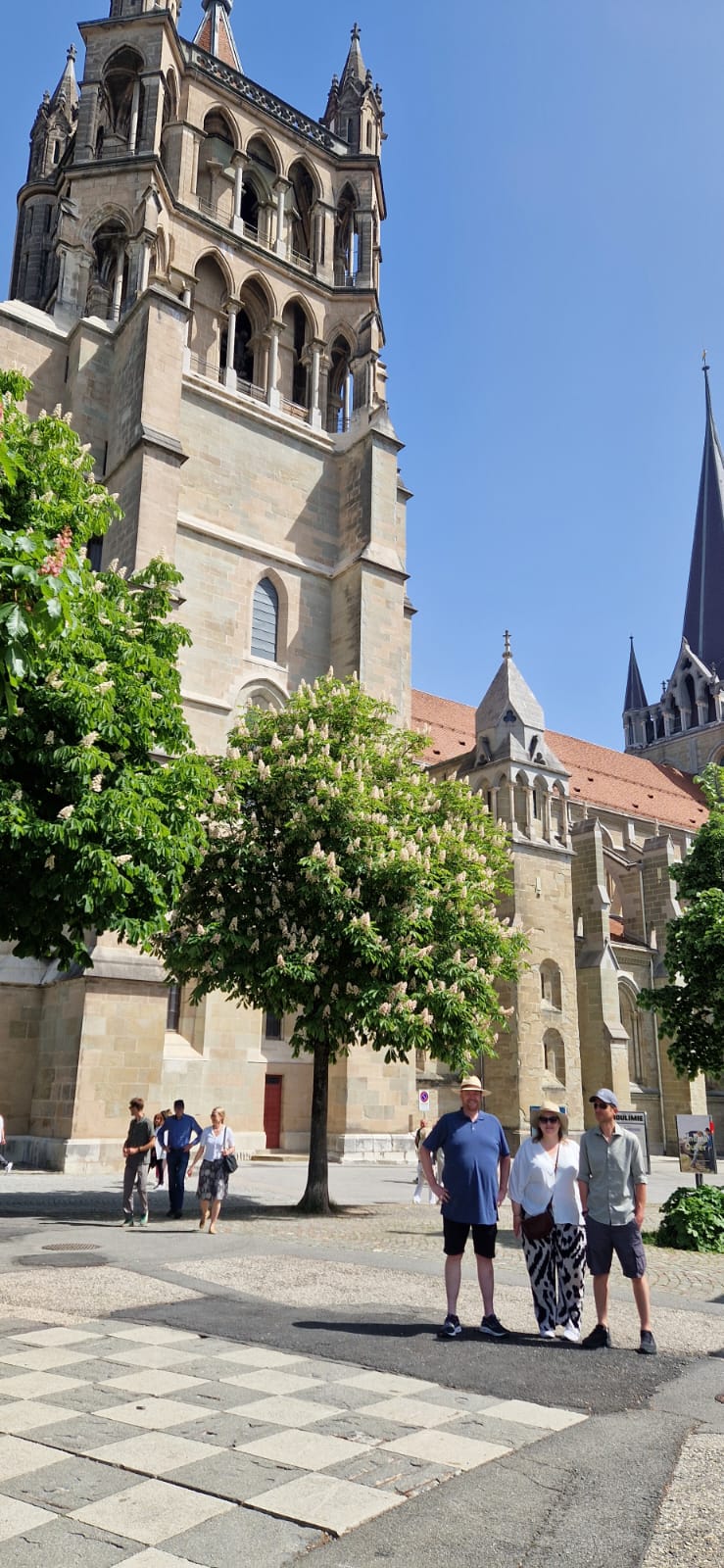 Historic building with tower, people, trees, and clear sky in urban environment.
