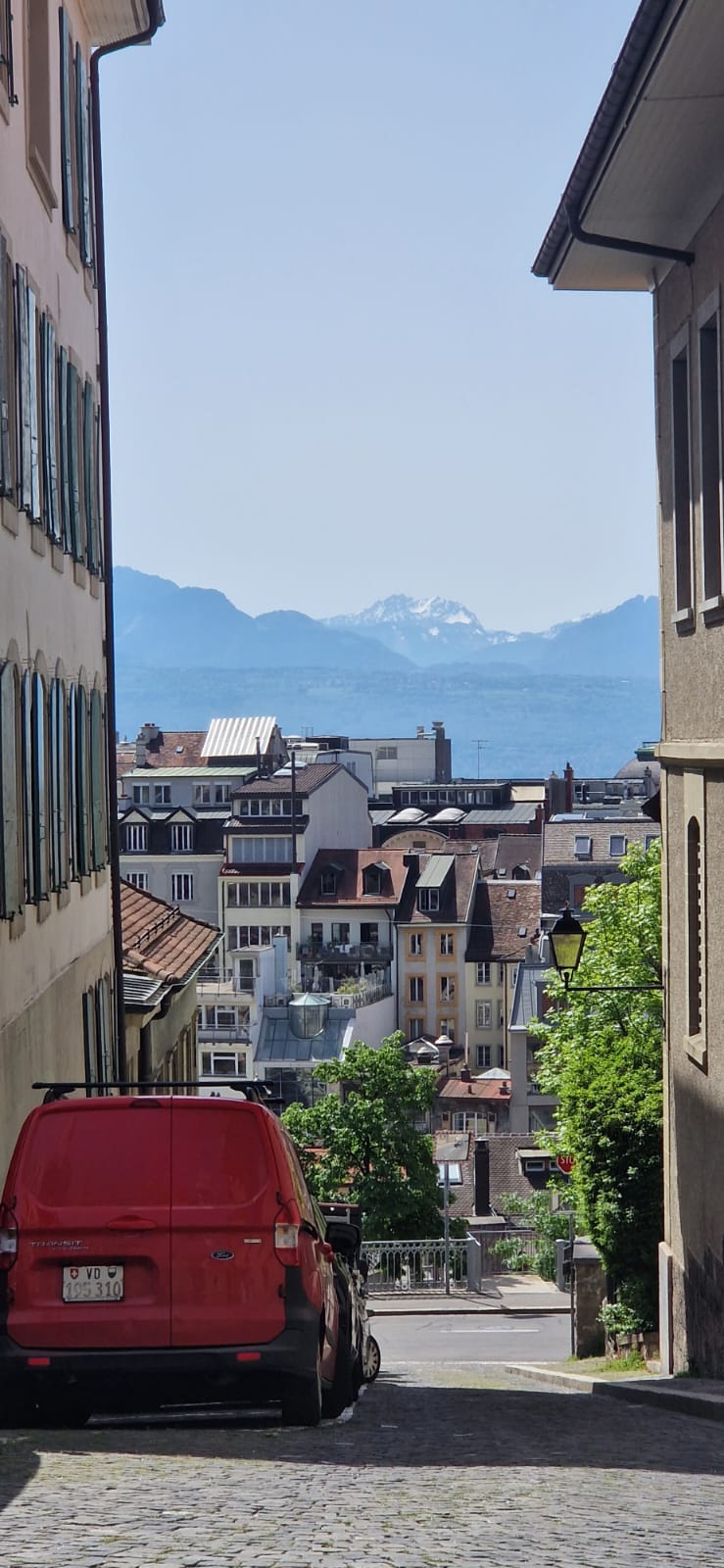 Cobblestone Street with Mountain View Narrow downhill street with red van, buildings, and distant mountains.