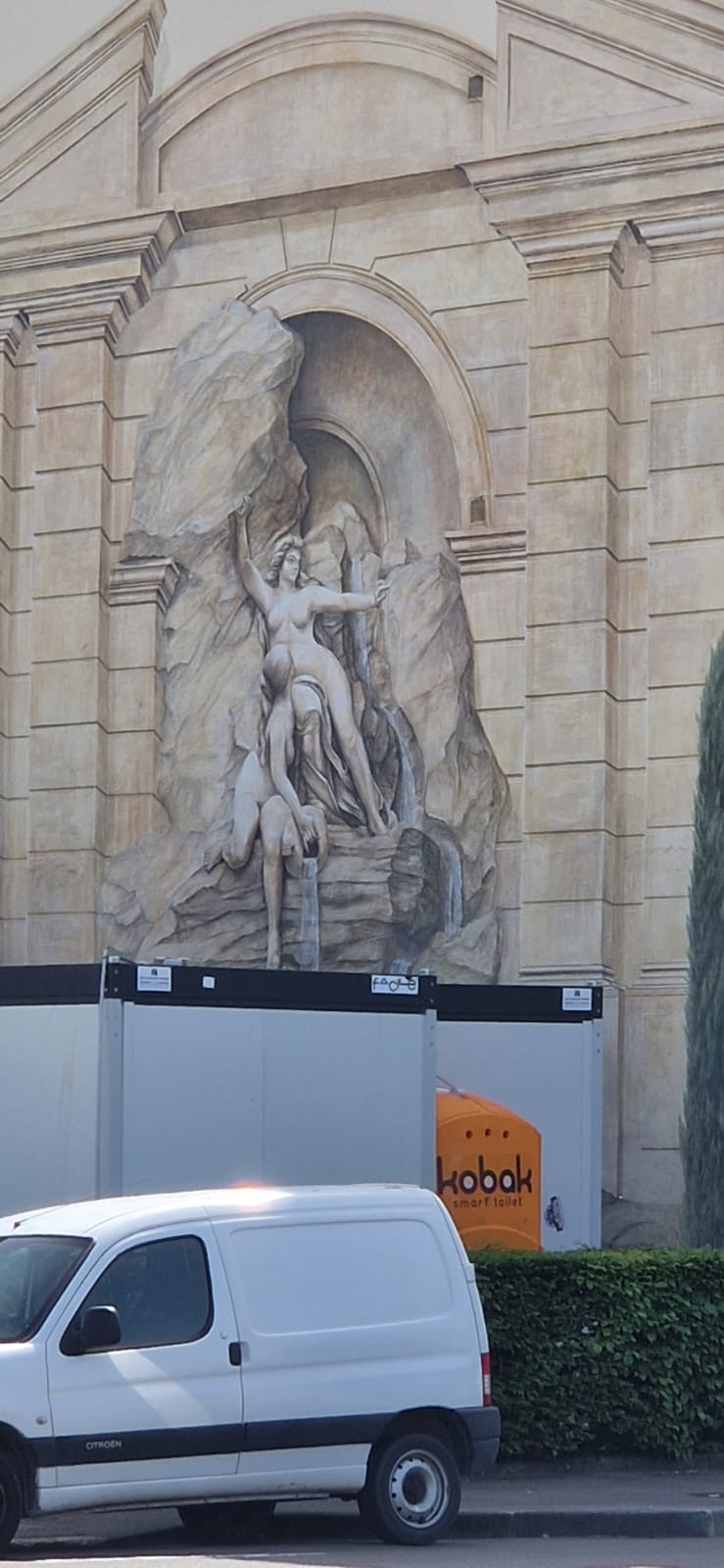 Classical Mural with Modern Interruptions Detailed mural showing classical scene with nude figures, stone archway, van, and portable toilet.