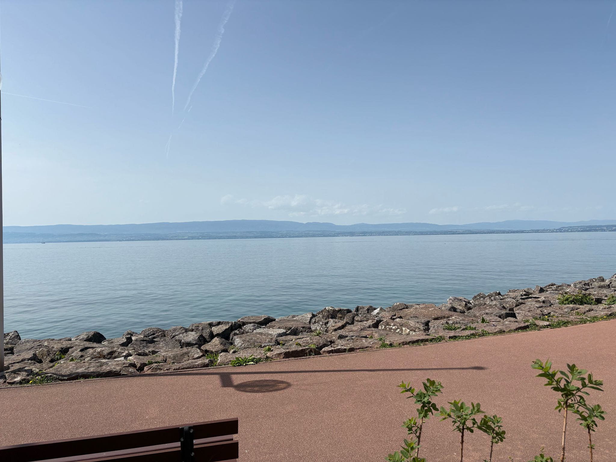 Waterfront scene with rippling water, rocky shoreline, clear sky, and distant hills.