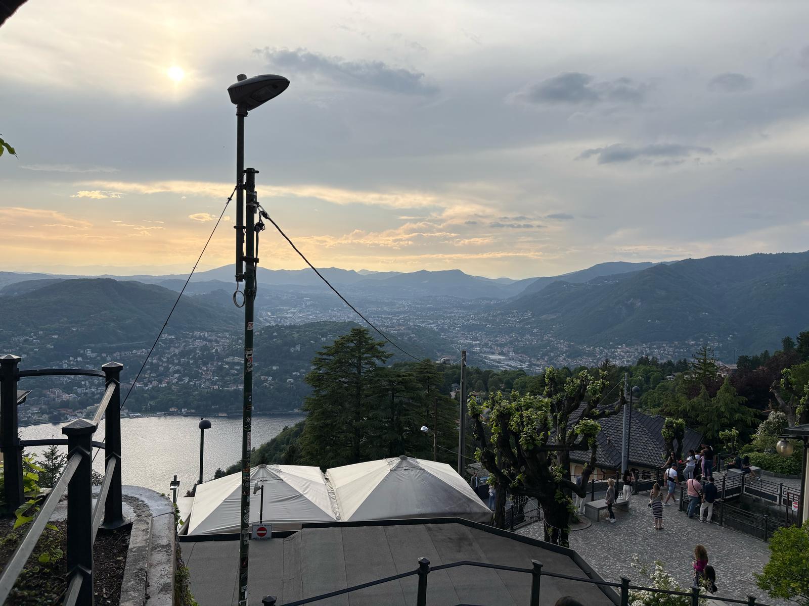 Sunset Vista Overlook Elevated scenic view of landscape, hills, water, sky, terrace with people, and lamppost.