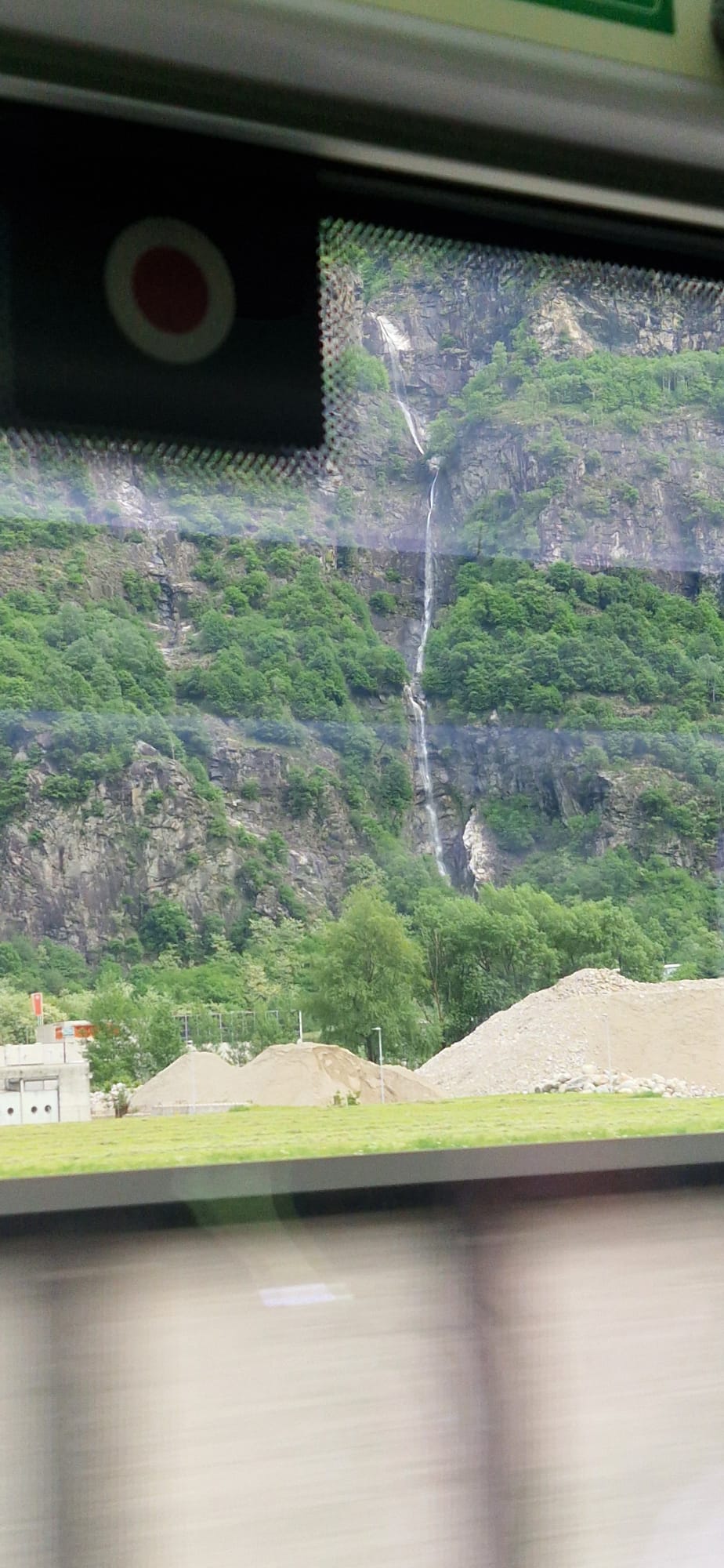 View of a tall waterfall on a forested hillside, with construction materials in the foreground.