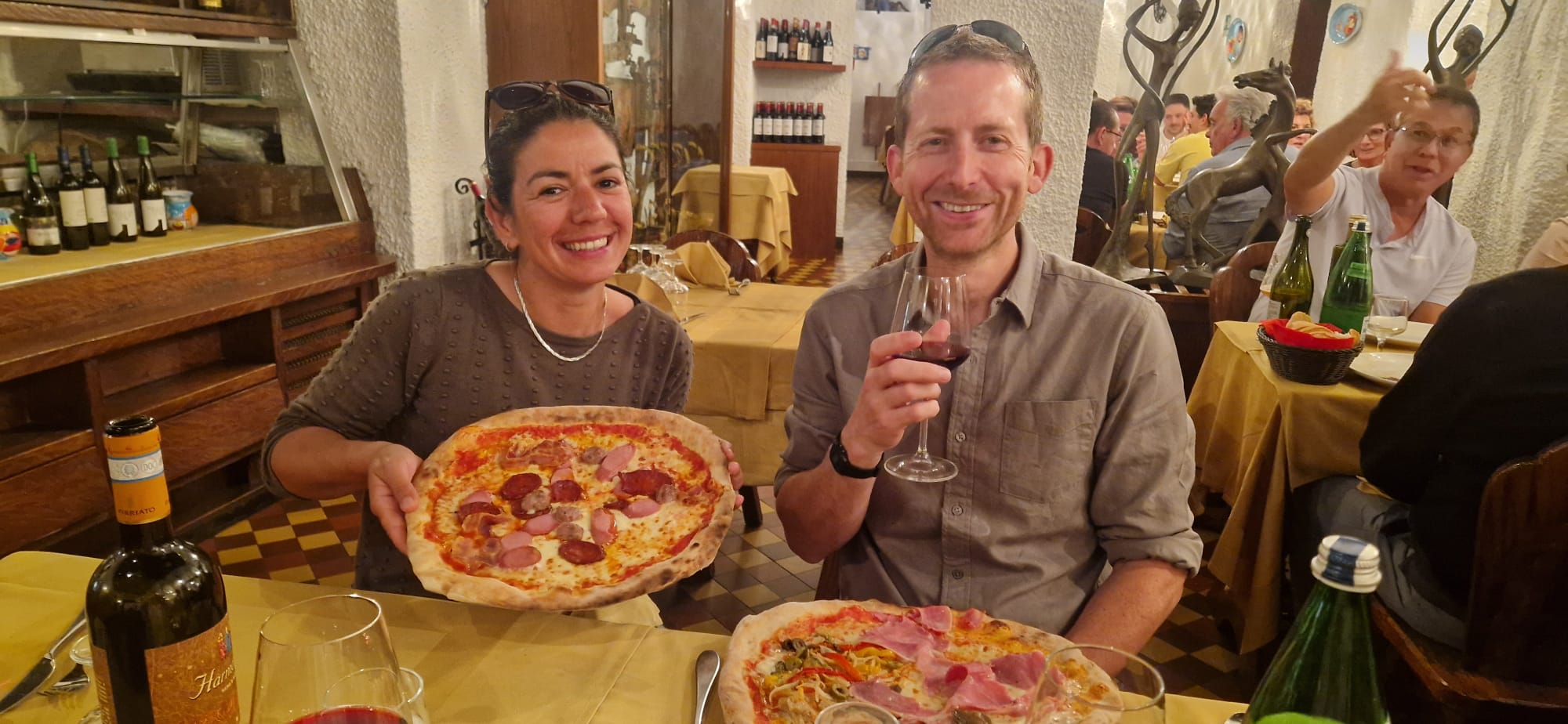 Pizza and Wine Dinner Duo Two people dining at a restaurant with pizza and wine, surrounded by a warmly lit setting.