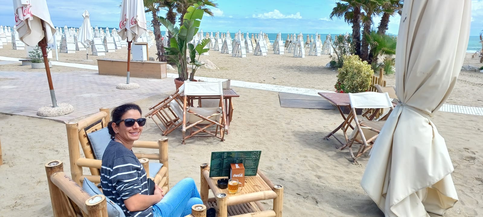 Beachside Relaxation with Palm View Person on beach in sunglasses, striped sweater and jeans, with bamboo furniture and sea view.
