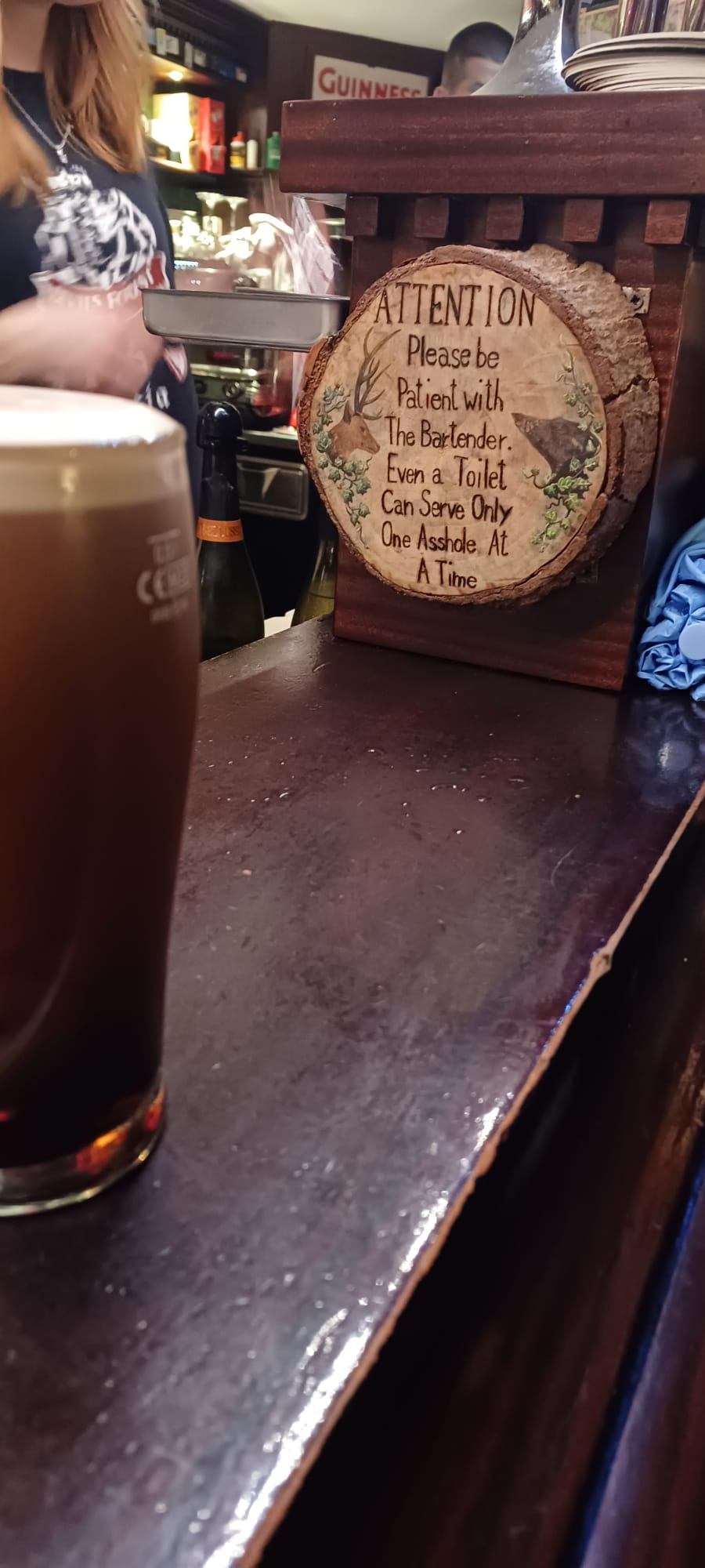 Dark Brew at Rustic Bar Counter Pint of dark beer on a bar with carved wooden sign and bottles in the background.