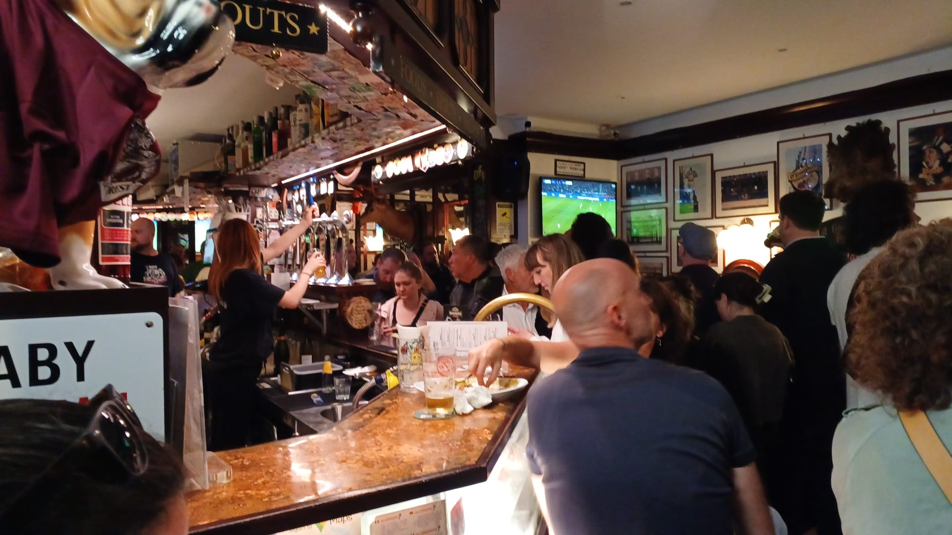 Lively Bar Scene with Sports Broadcast Crowded bar with people socializing, drinks, and a sports event on TV. Warm lighting.