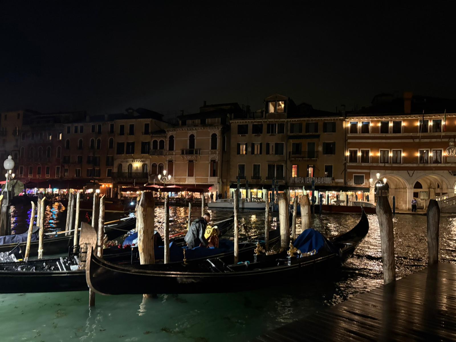 Nighttime Venice canal with moored gondolas and warmly lit buildings reflecting on water.