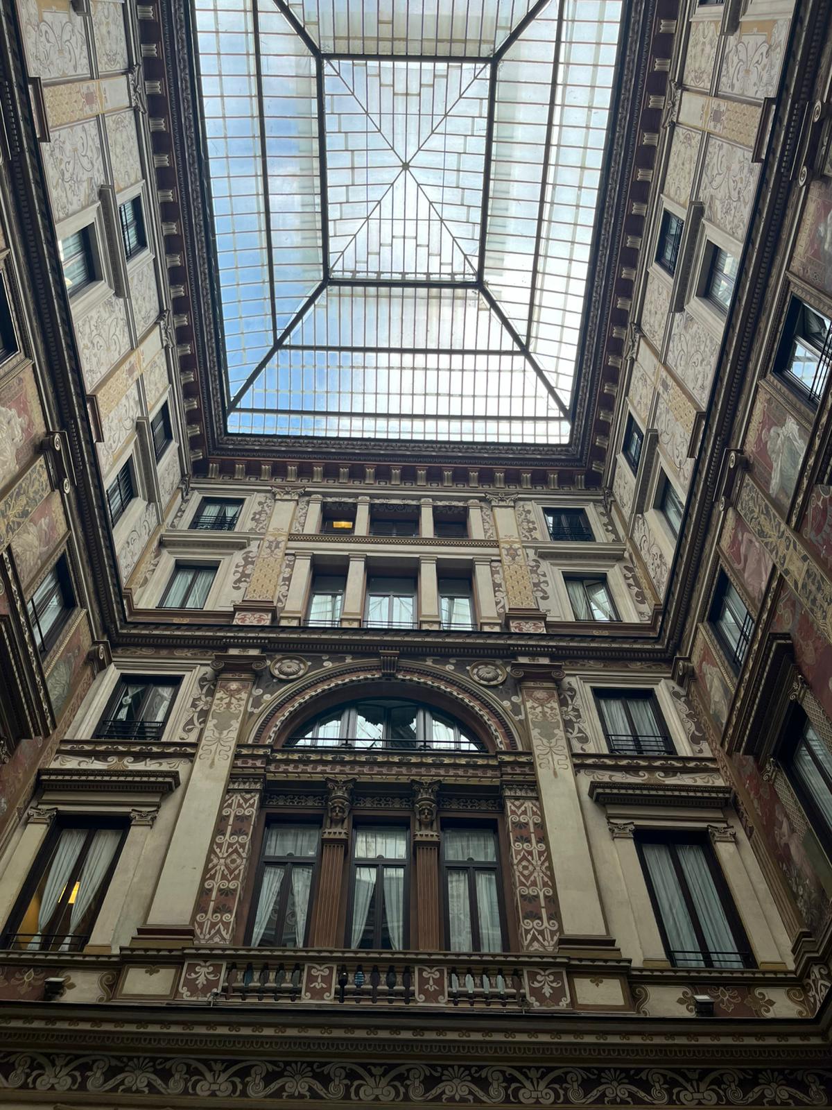 Ornate Multi-Story Atrium with Glass Ceiling Multi-story building interior with ornate architecture, glass ceiling, decorative windows, arches.
