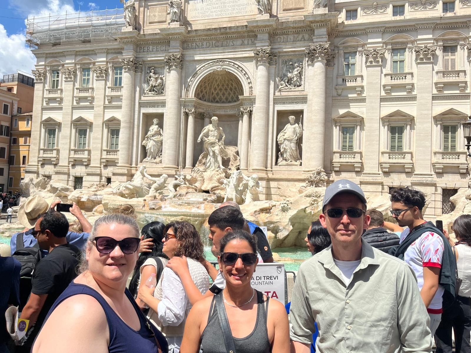 Group of tourists at Trevi Fountain, Rome with Baroque sculptures and flowing water backdrop.