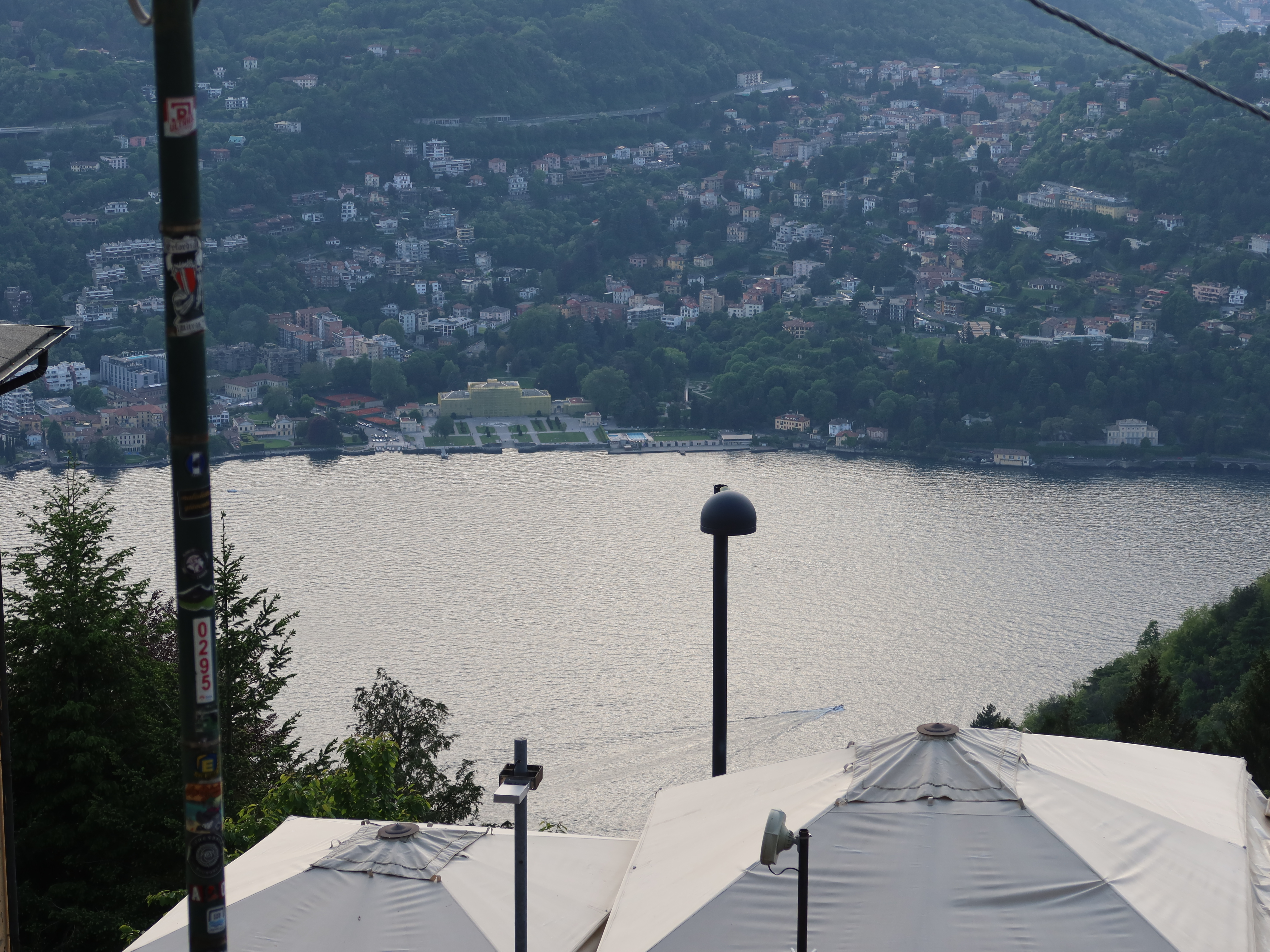 Scenic view over water with distant buildings, forested hills, tents, and sticker-covered pole.