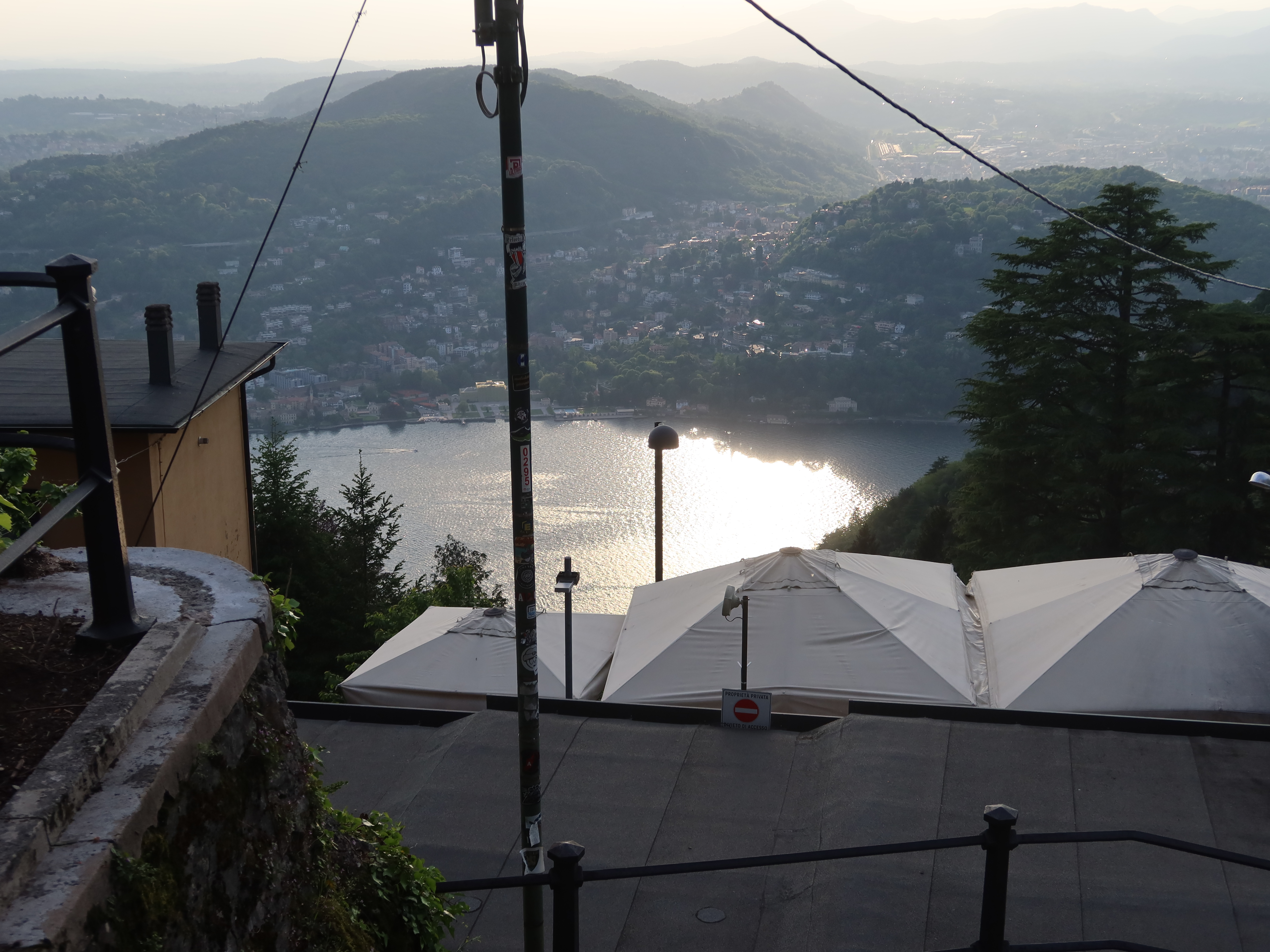 Scenic view of lake, hills, town, rooftop with canopies, utility pole, and sunlight reflection.