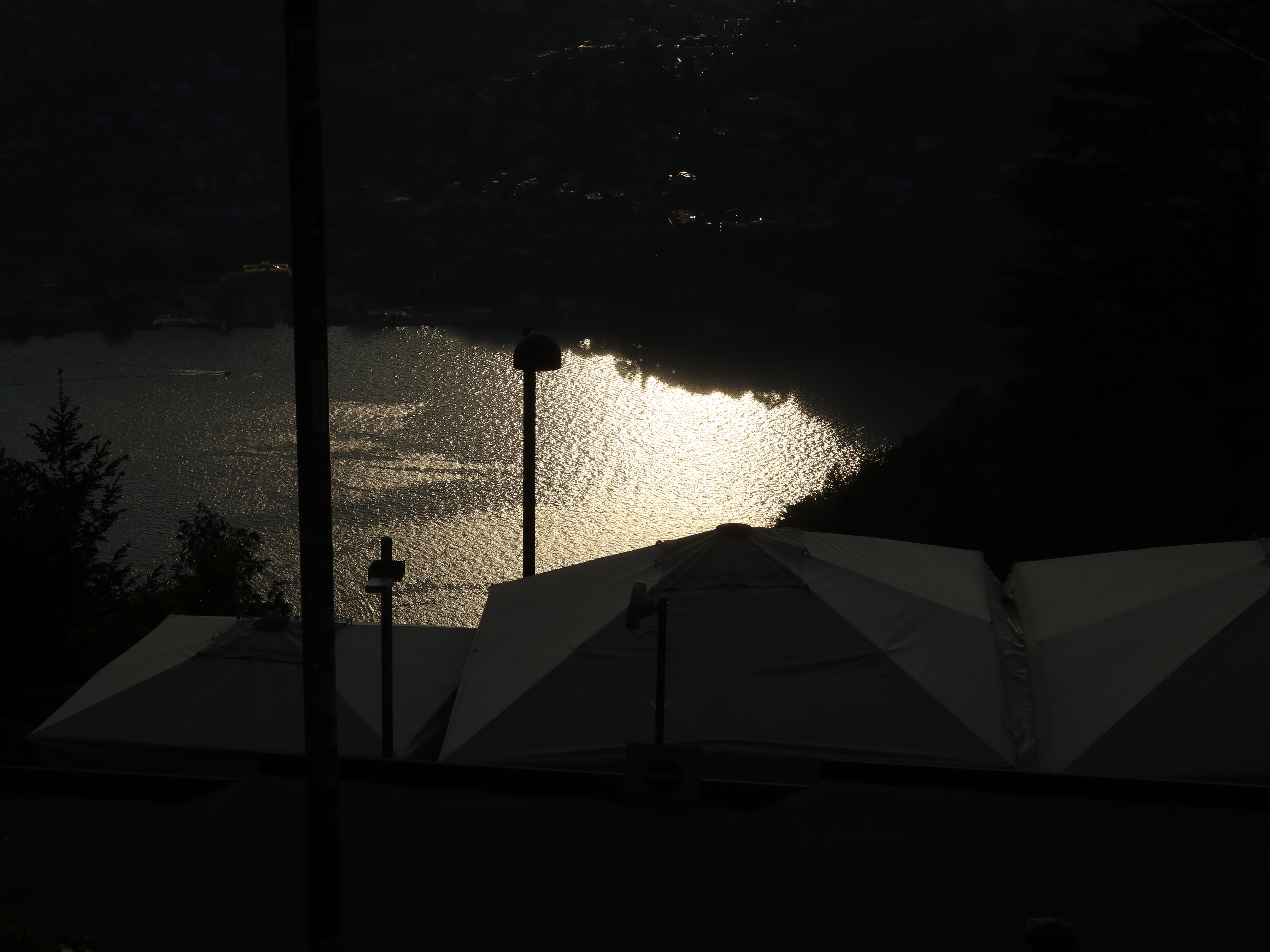 Lakeside Sunset Reflection Large body of water reflecting sunlight, with tents and poles silhouetted in the foreground.