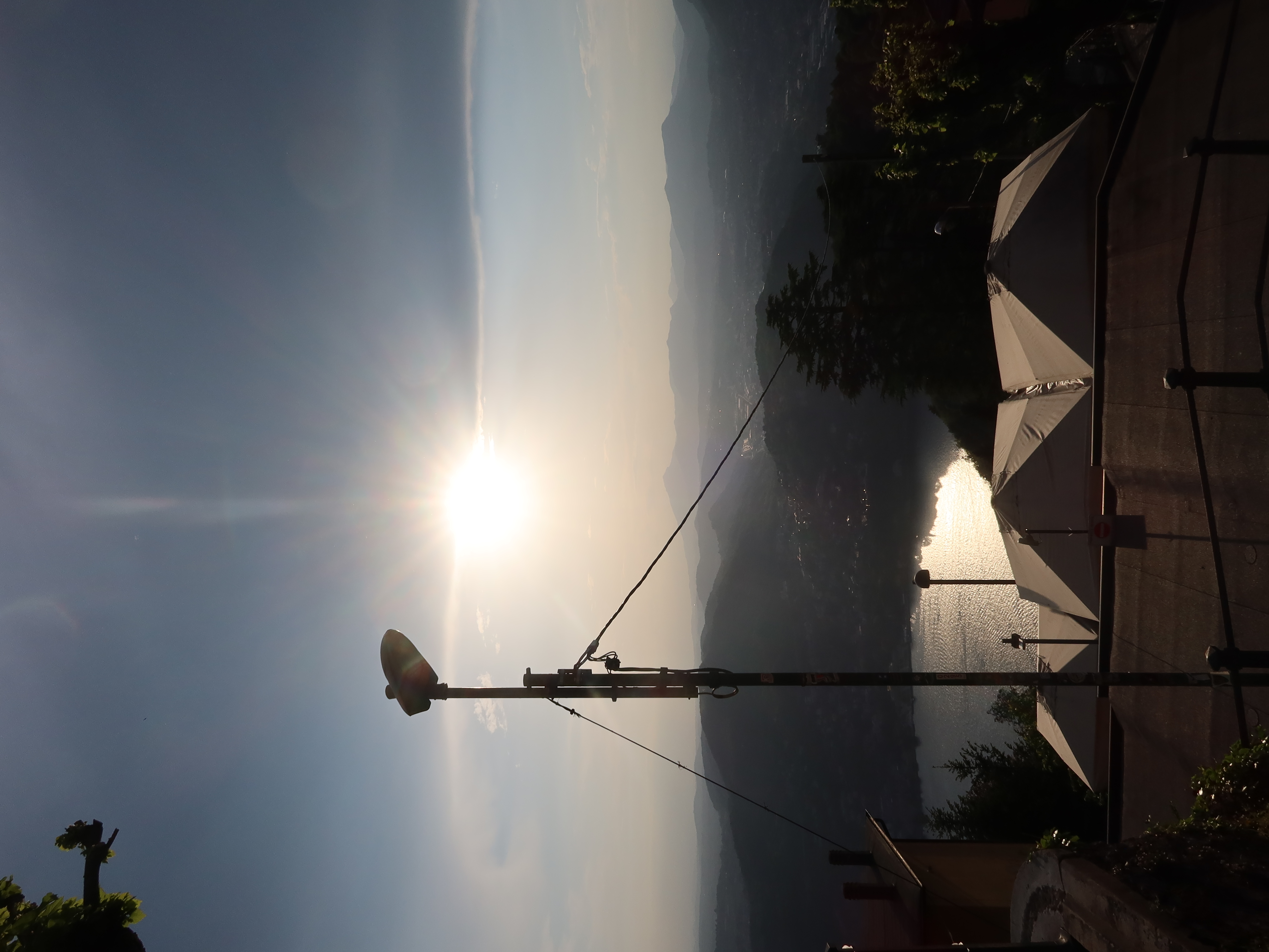 Scenic sunset over mountains with sunlit water, silhouetted roofs, and streetlight in foreground.