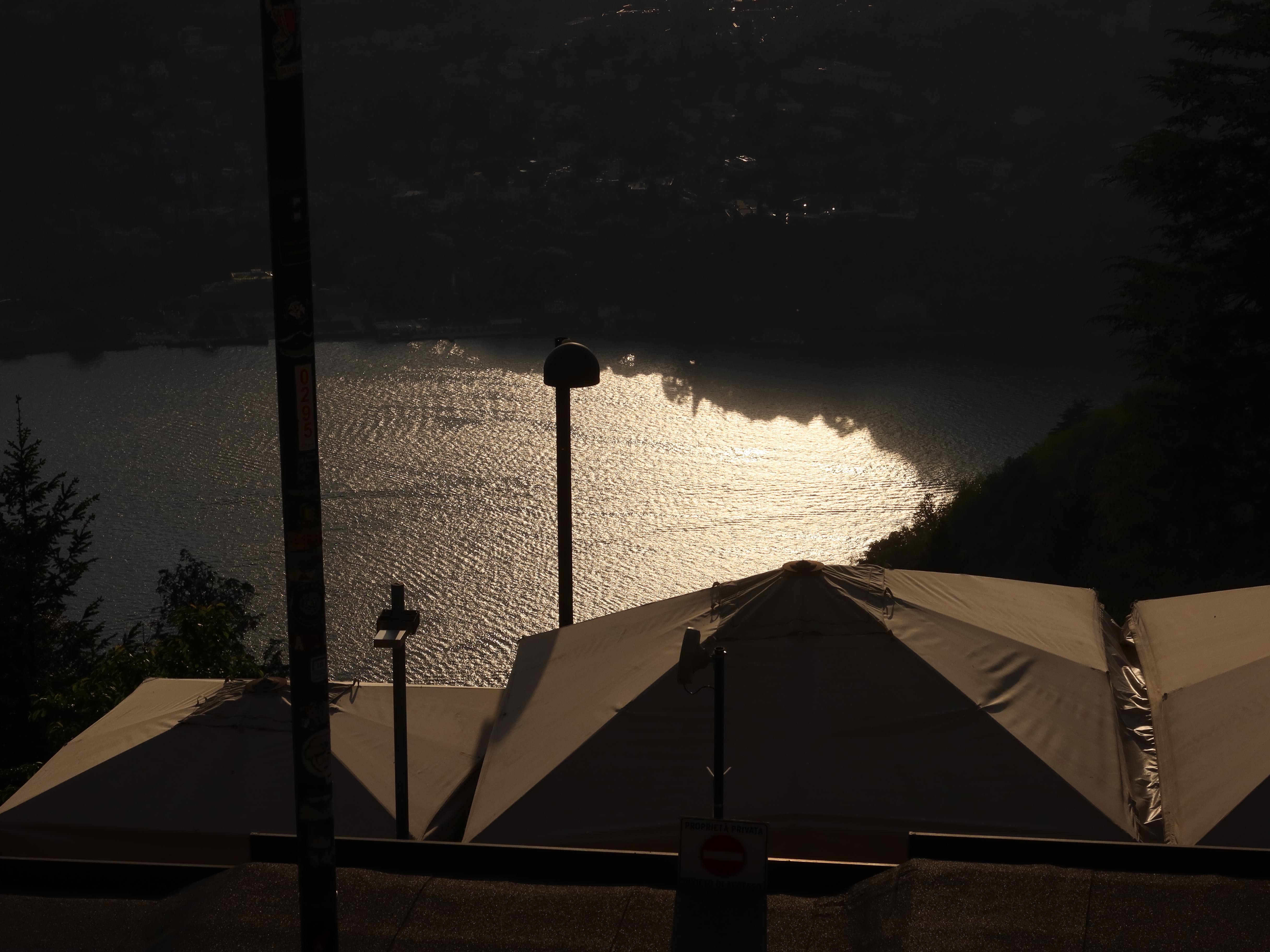 Lakeside sunset with shimmering water, silhouetted tents, and darkened surroundings.