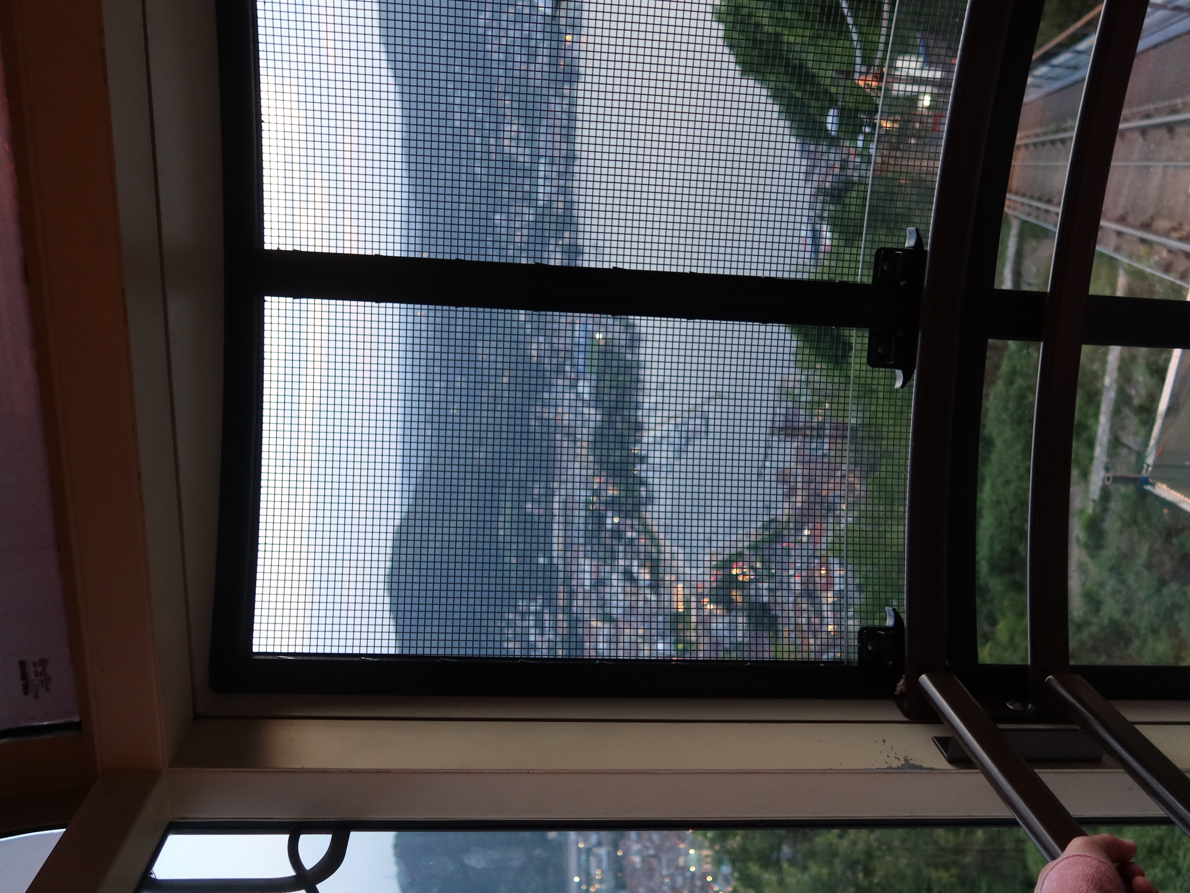 View from cable car with mesh screen, showing cityscape, water, hills, and railway tracks.