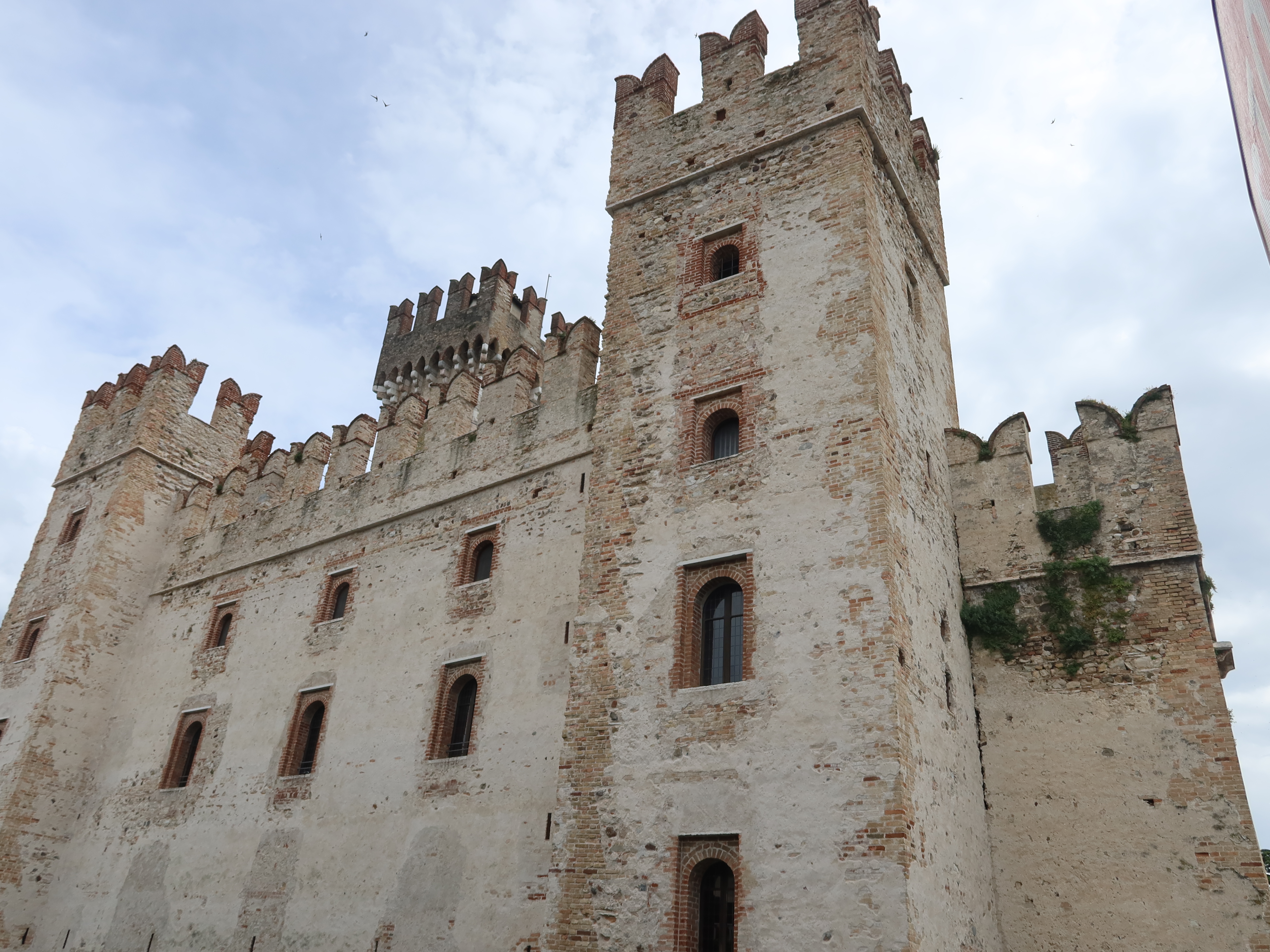 Medieval stone castle with crenelated towers, arched windows, and rough, weathered surface.