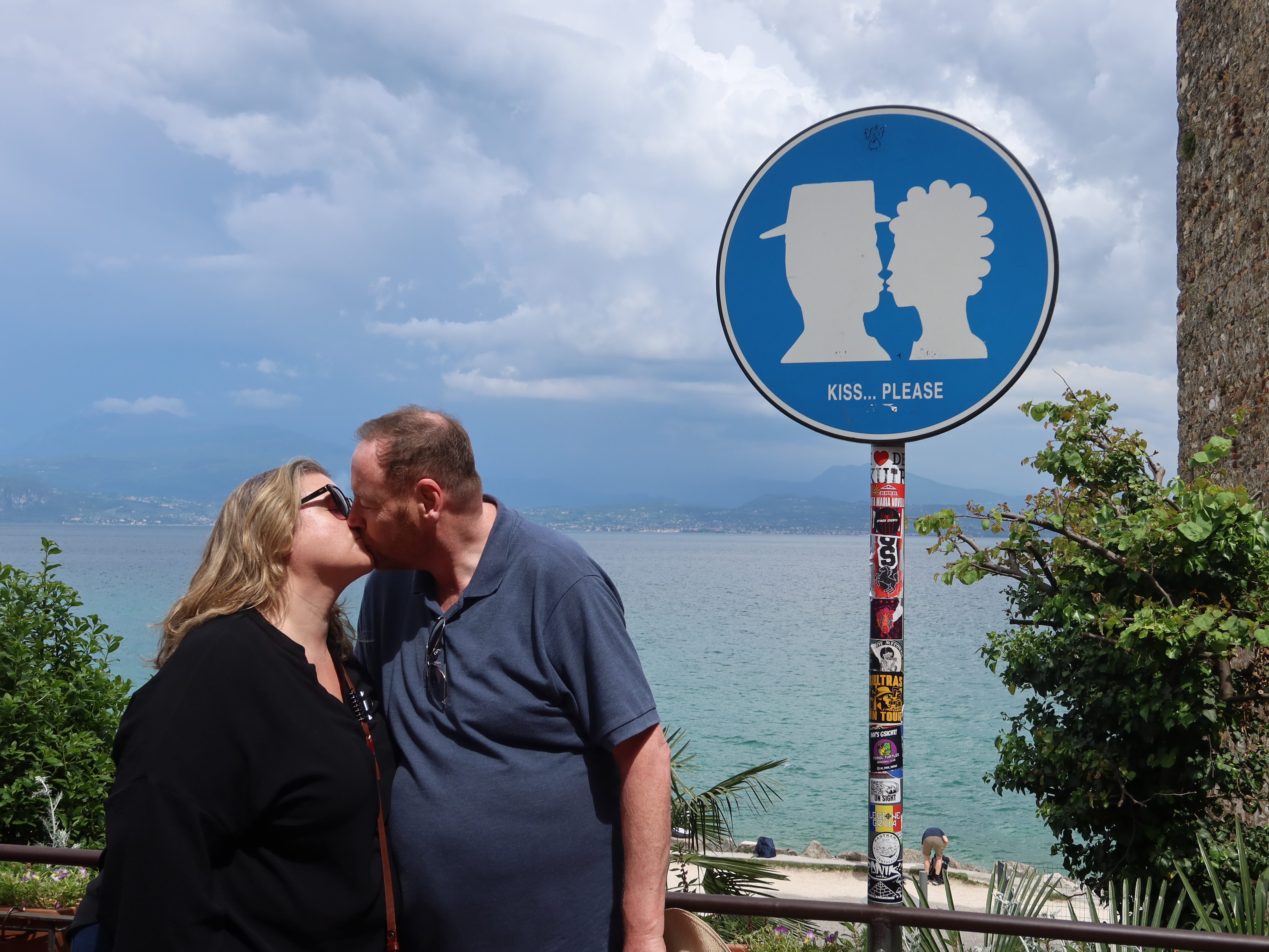 Romantic Moment by Scenic Sign Couple kissing by sign with silhouettes and "Kiss... Please," scenic water view in the background.