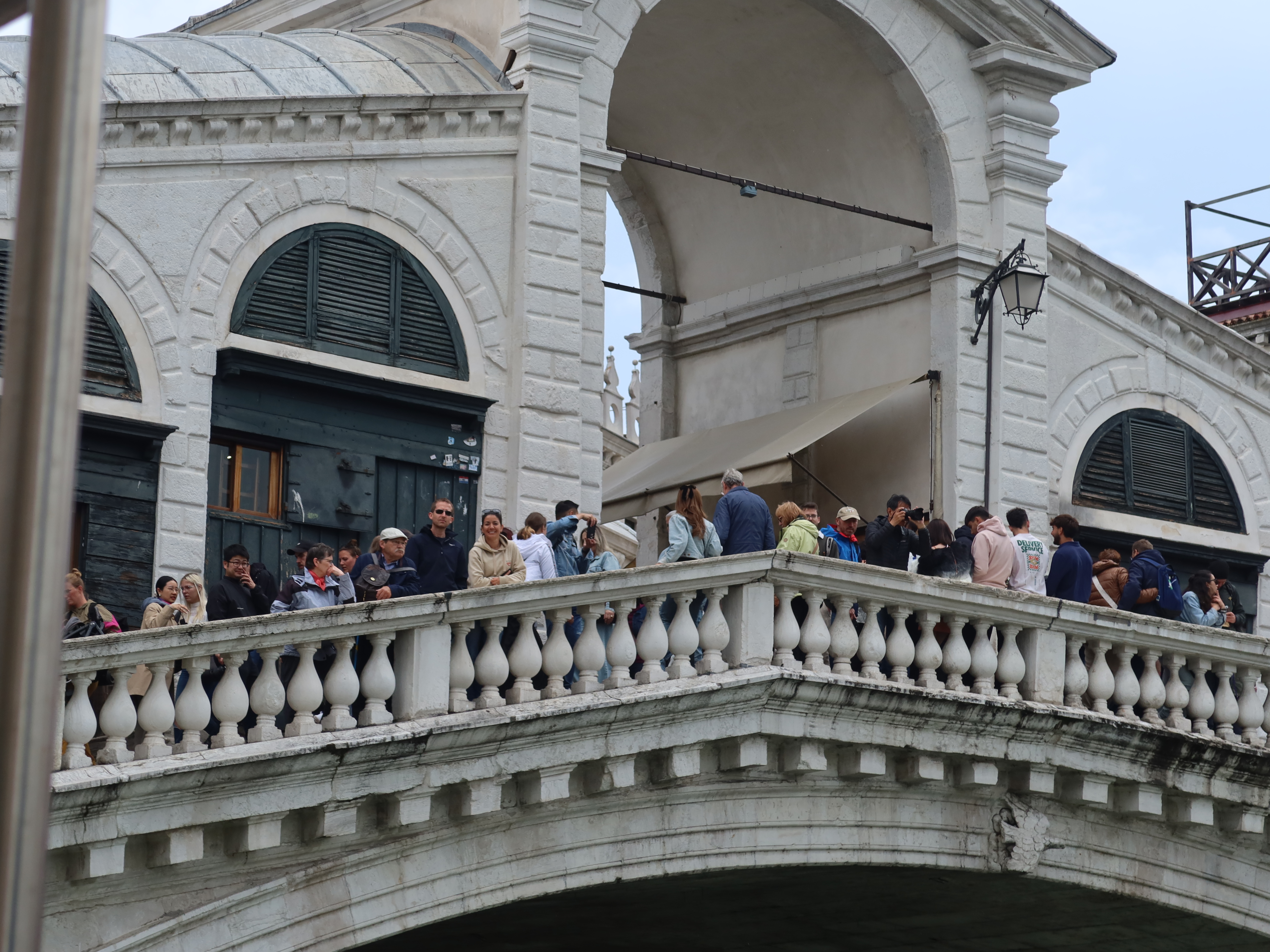 People on an ornate white stone bridge with arches and balustrades, near historic building.