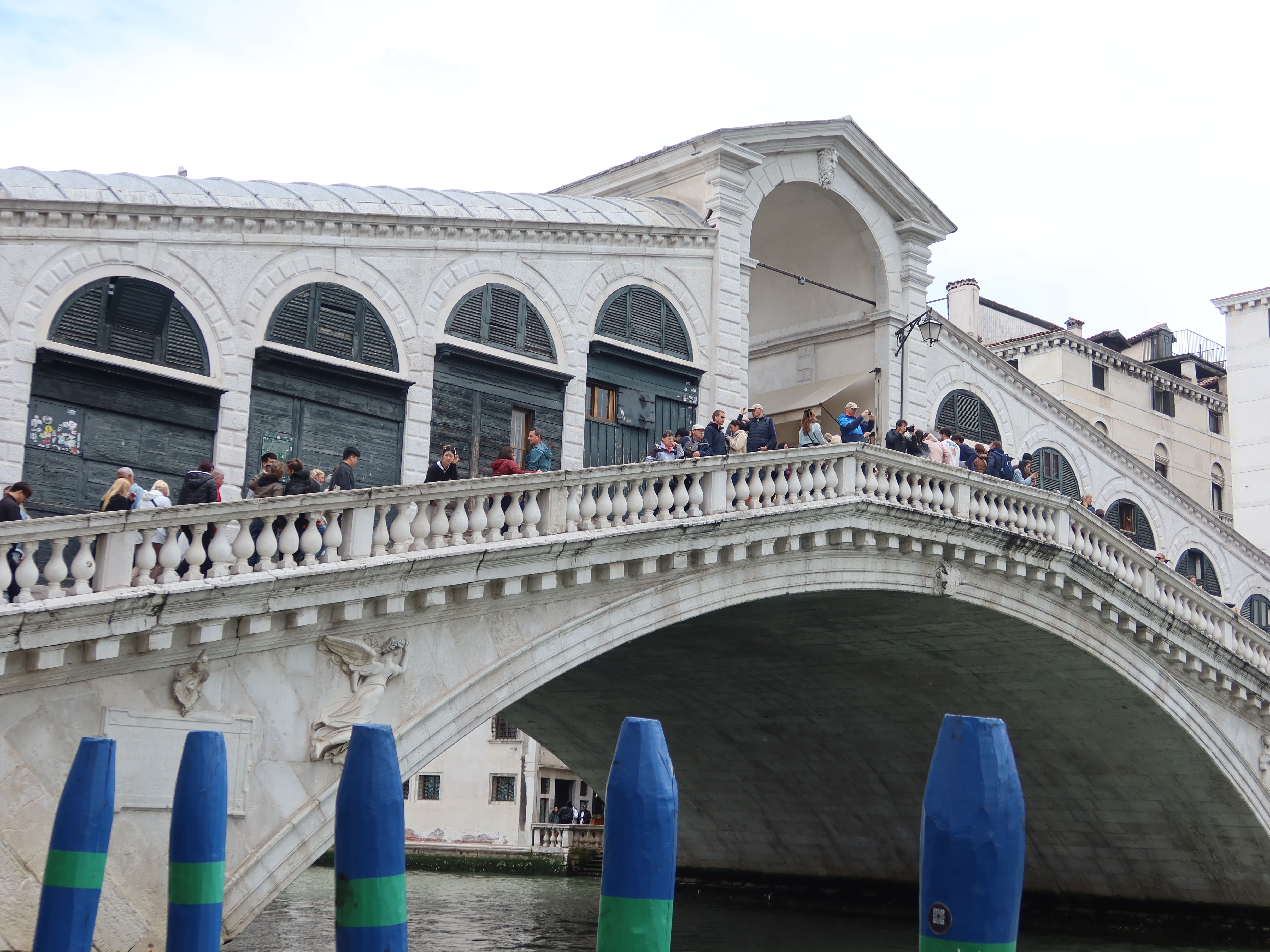 Rialto Bridge in Venice, Italy with people, arches, and striped posts over a canal.