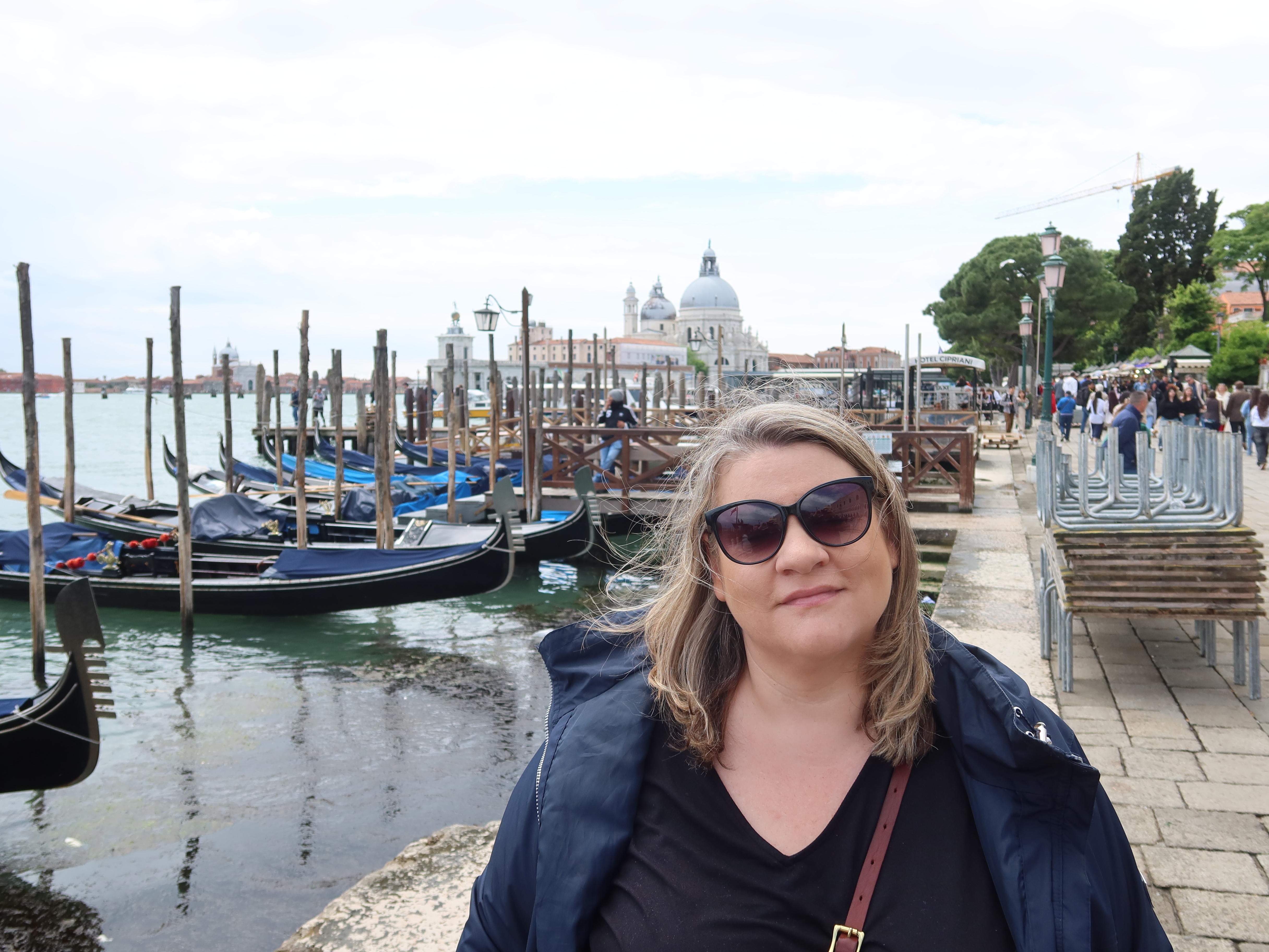 Gondolas by the Waterfront Woman in sunglasses near waterfront with gondolas, historical buildings, trees, and people.