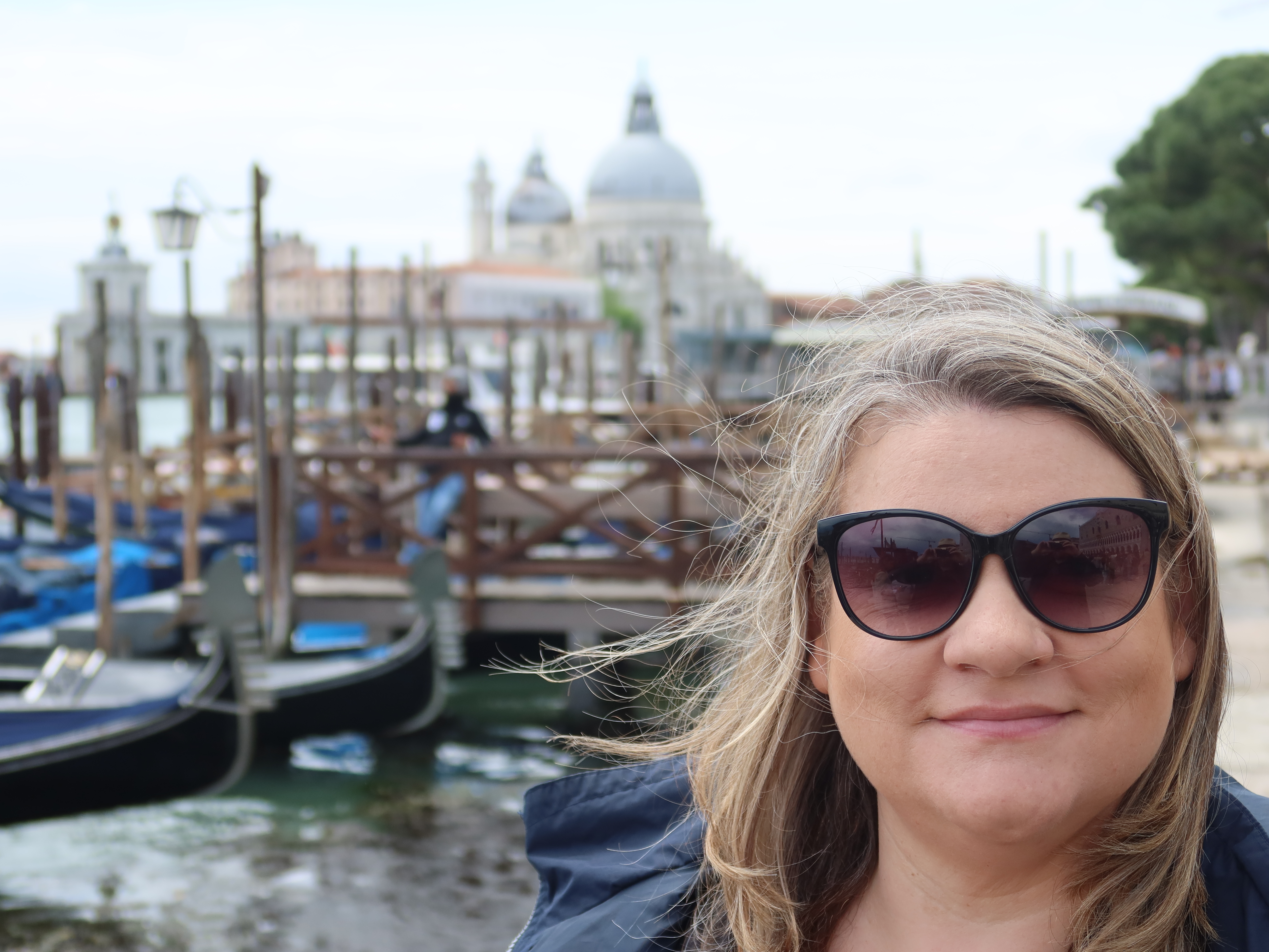 Person in sunglasses with gondolas and historic dome in the blurred background.