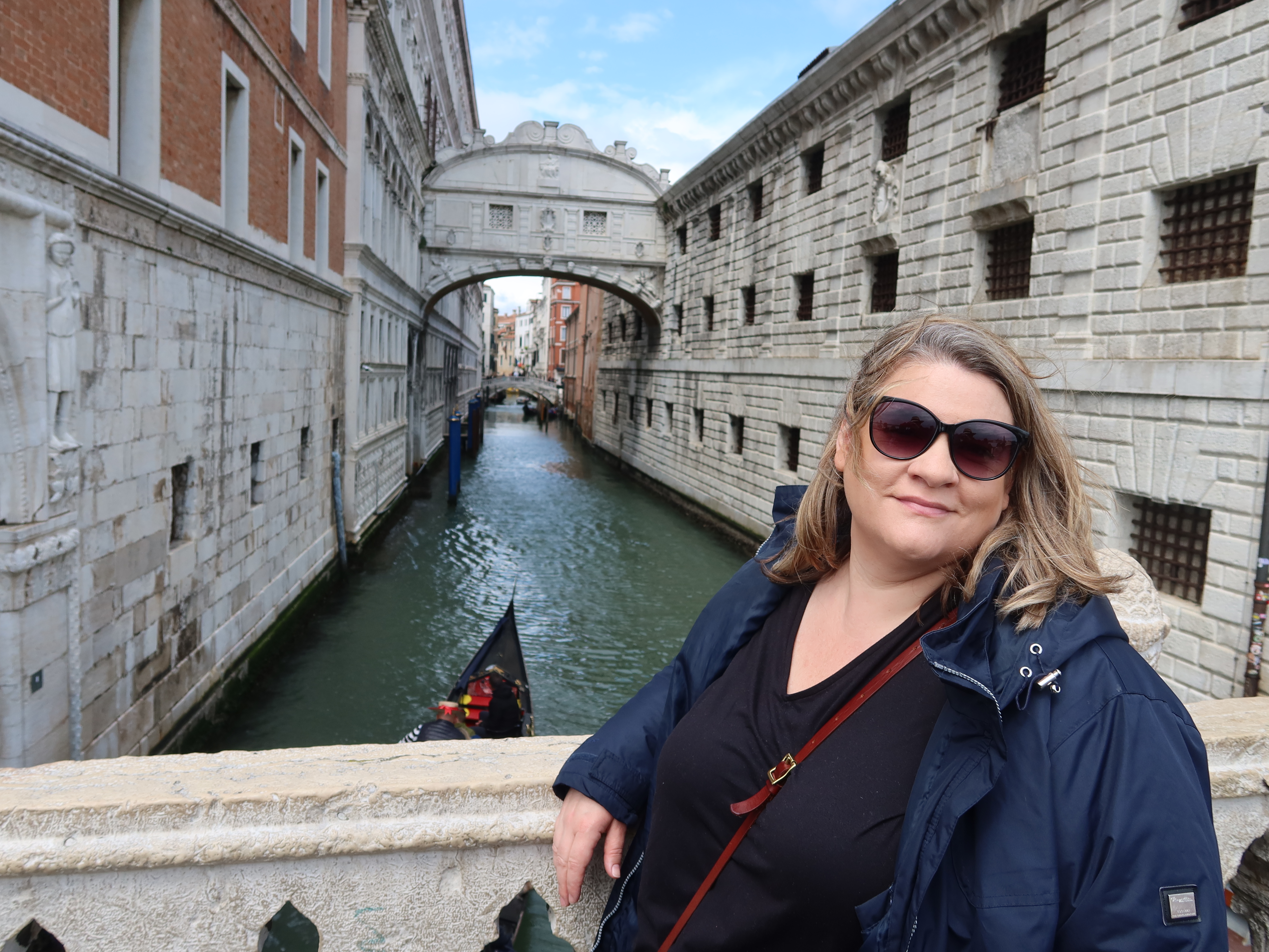 Person in sunglasses on a bridge in Venice, with a canal and the Bridge of Sighs in view.