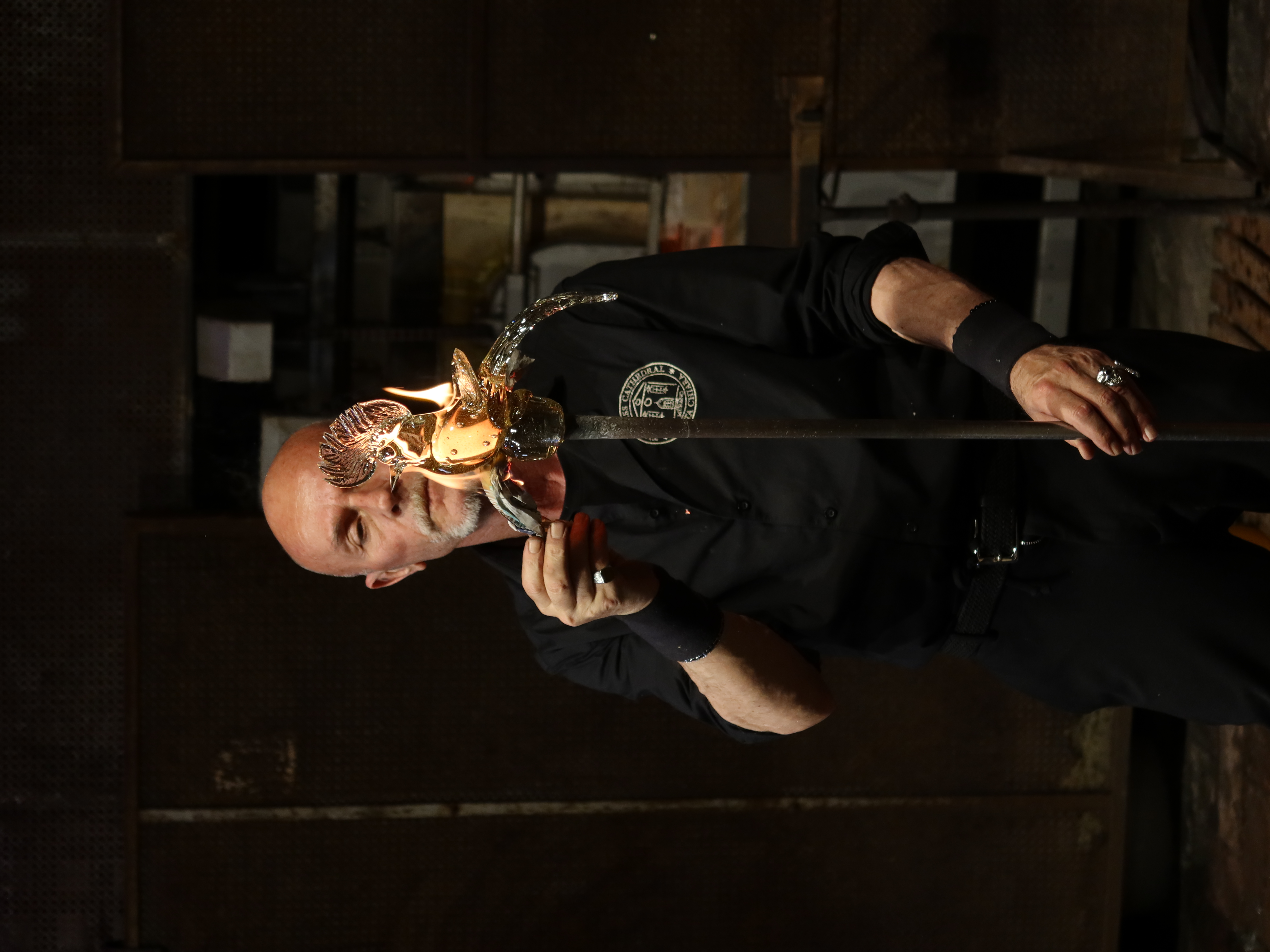 Person glassblowing a bird sculpture with flames in an industrial workshop setting.