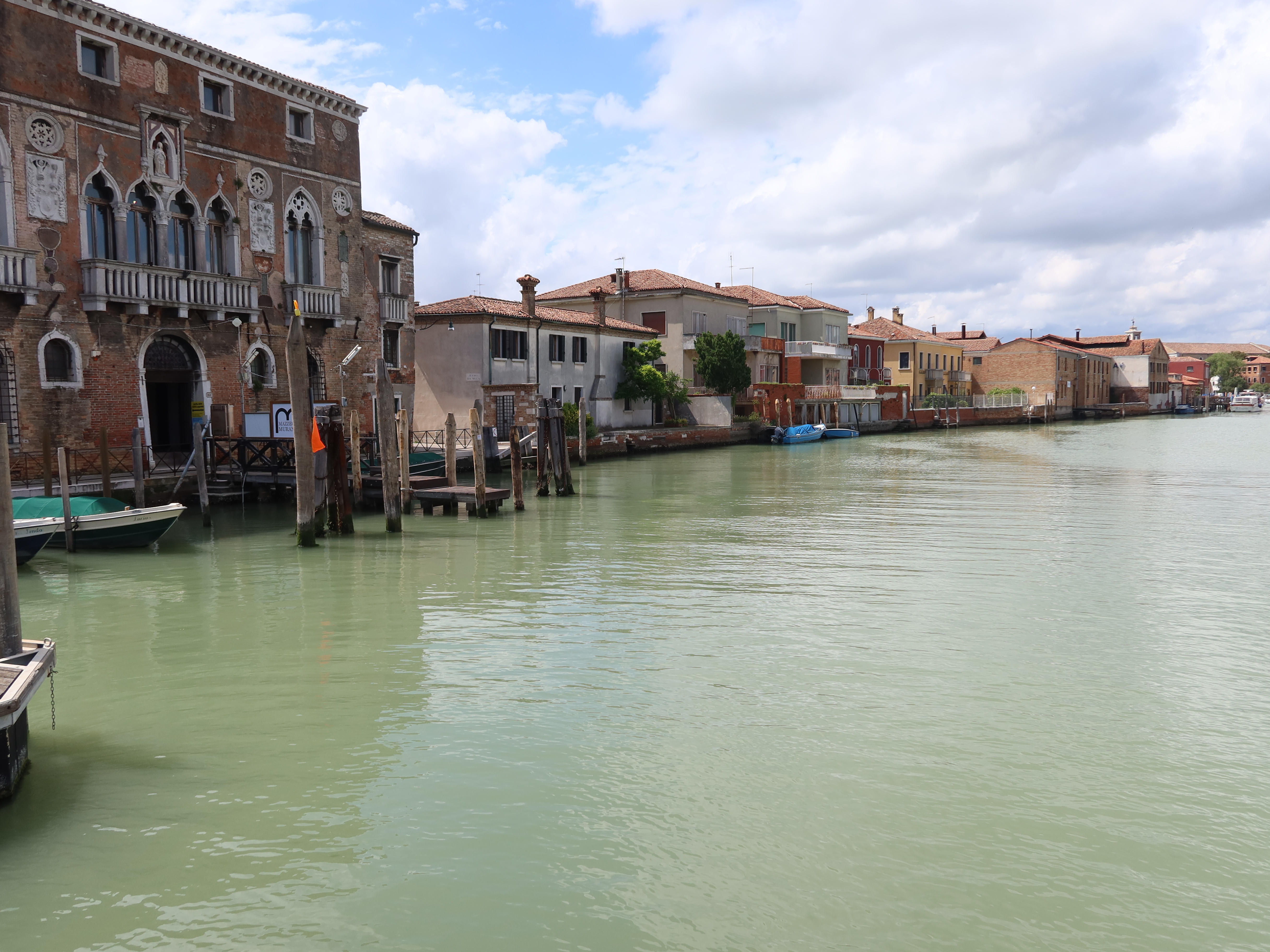 Canal with historic buildings, arched windows, and boats under a partly cloudy sky.