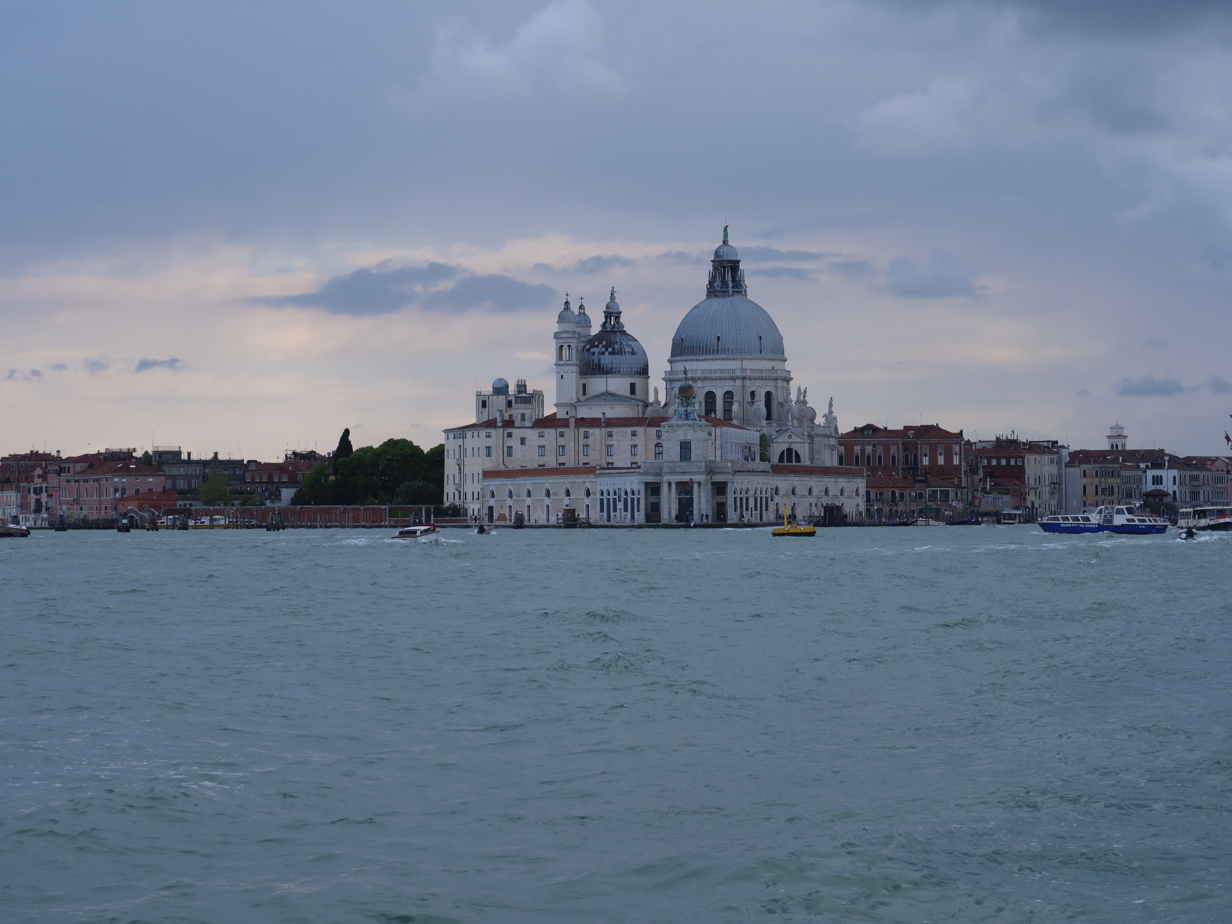 Large domed church by waterfront, cloudy sky, boats, cityscape with historic buildings in view.