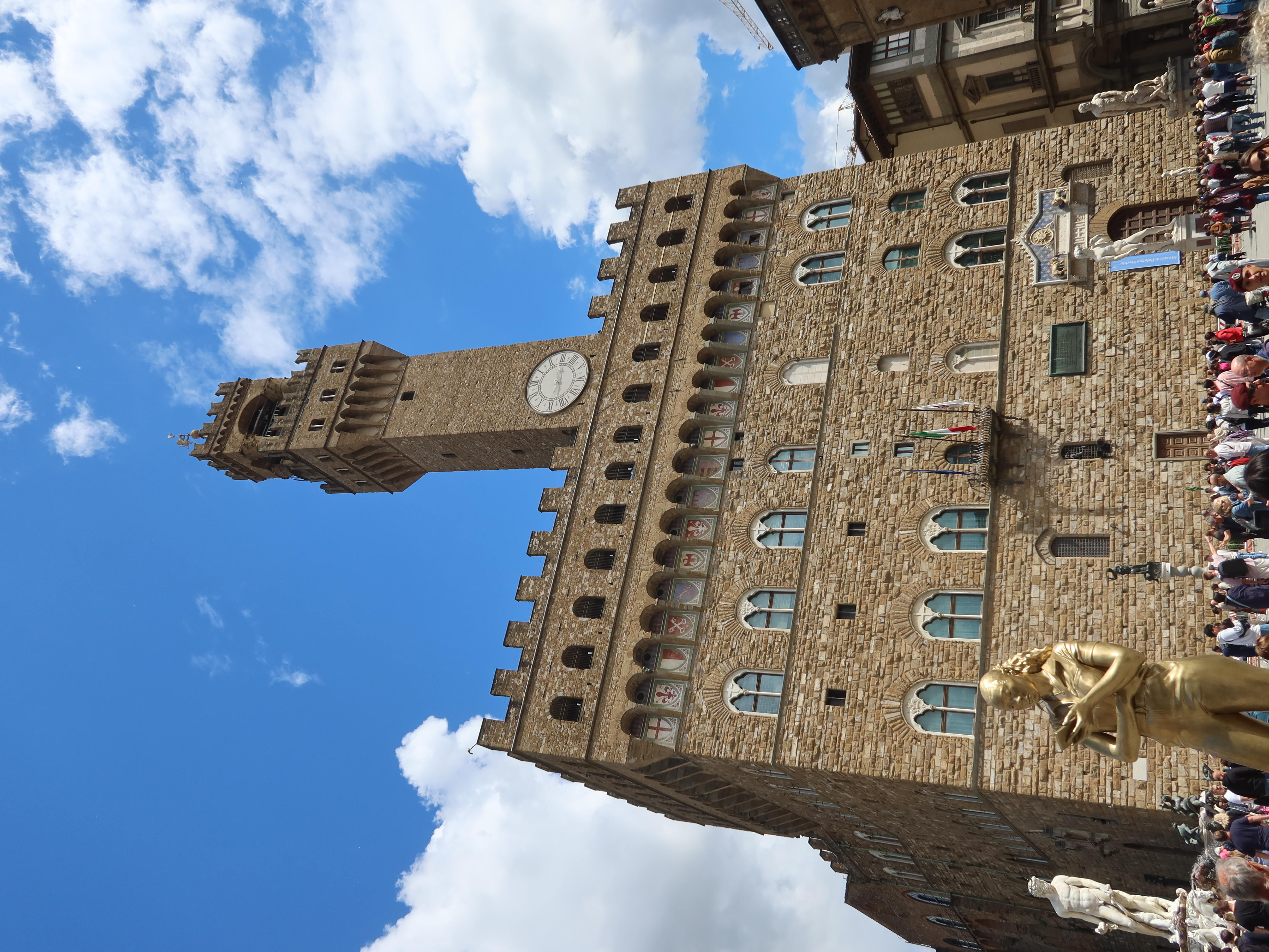 Palazzo Vecchio and Clock Tower with Plaza Crowd Palazzo Vecchio with clock tower, arch windows, crowd, statues, gold street performer, clear sky.