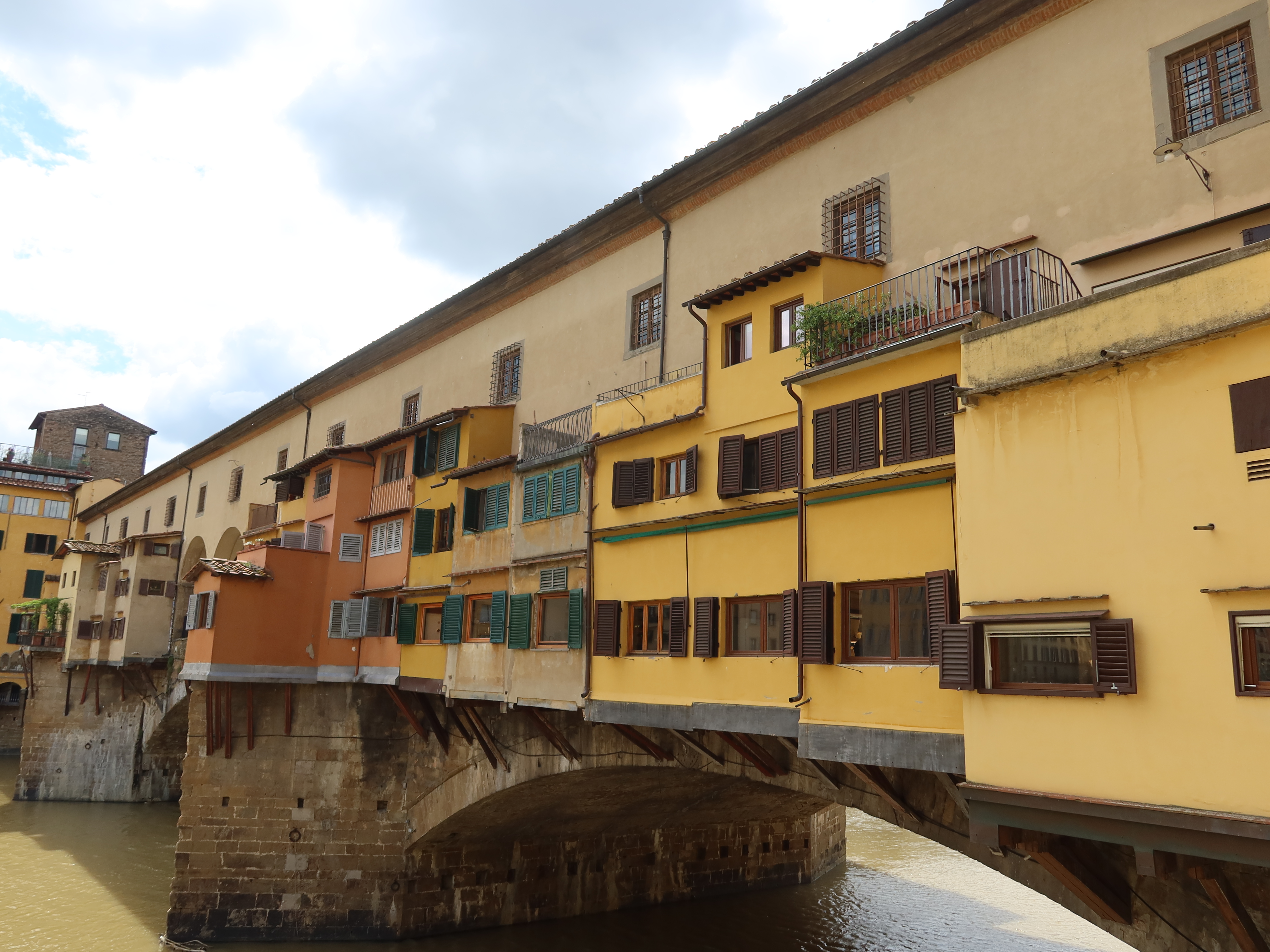 Ponte Vecchio in Florence with colorful shops and buildings over a river under cloudy skies.