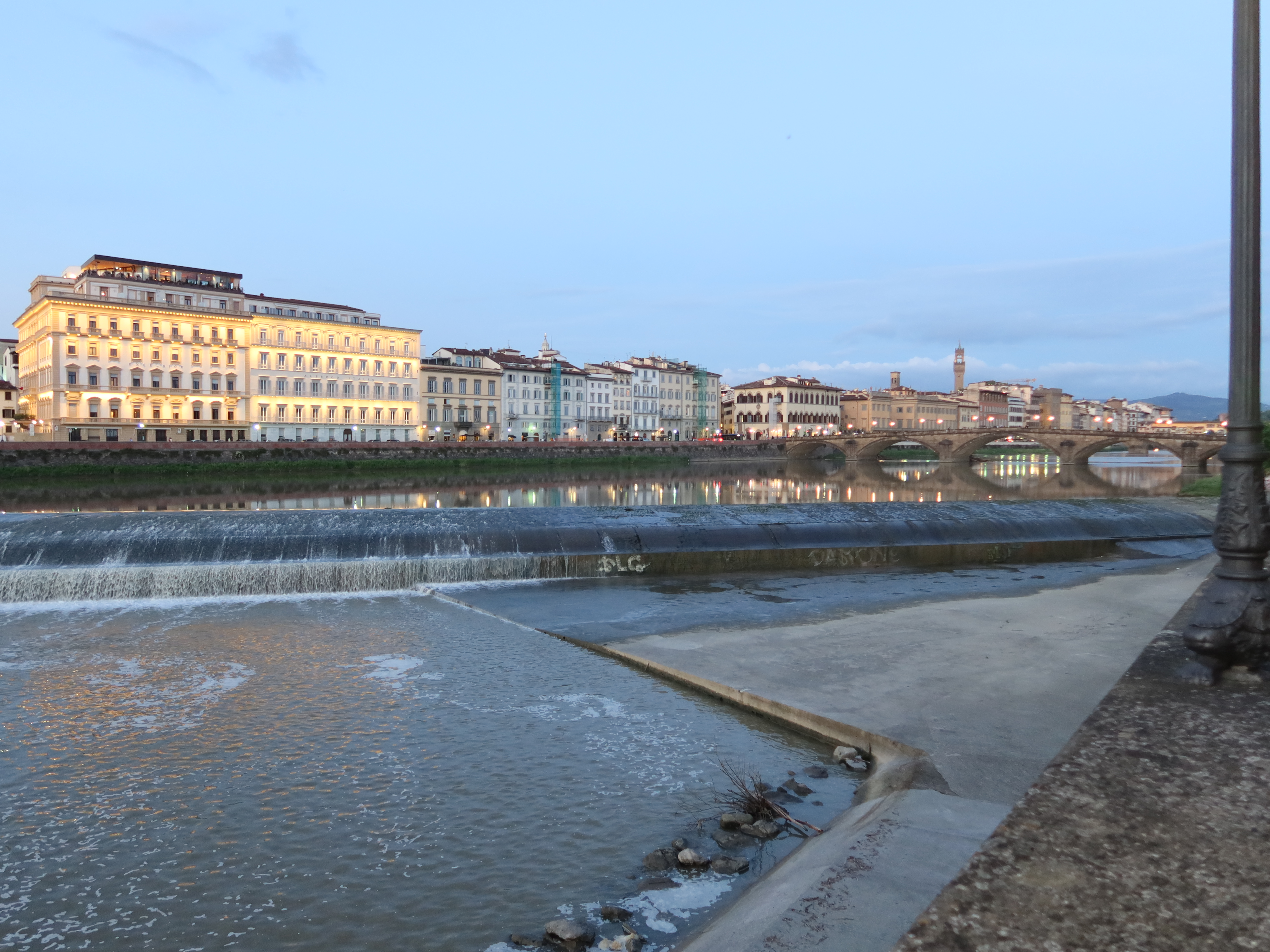 River in city with illuminated buildings and bridges at twilight, reflecting on water.
