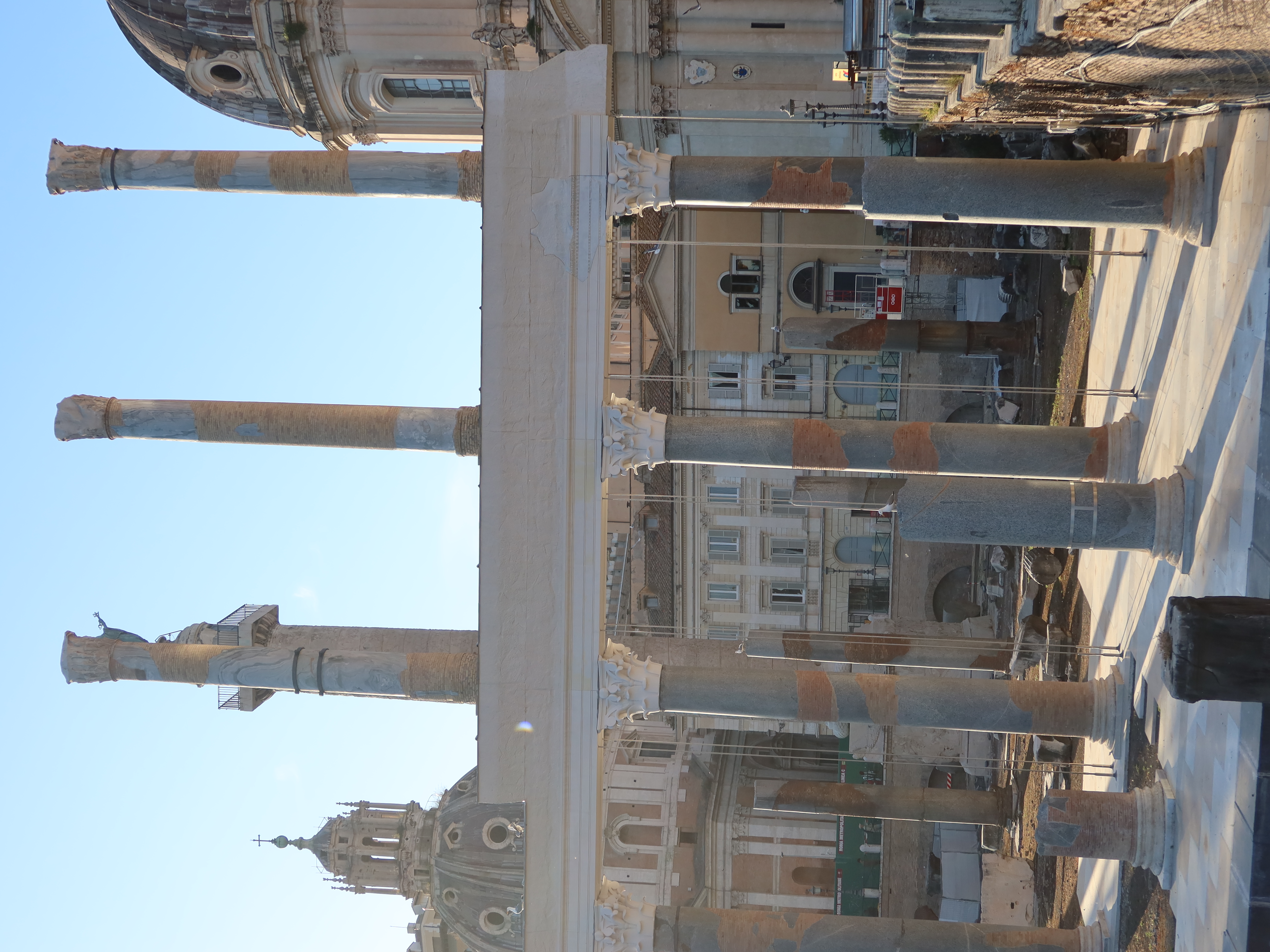 Ancient Columns at European Historical Site Ancient marble columns with repairs, flanked by historical domed buildings, late afternoon light.