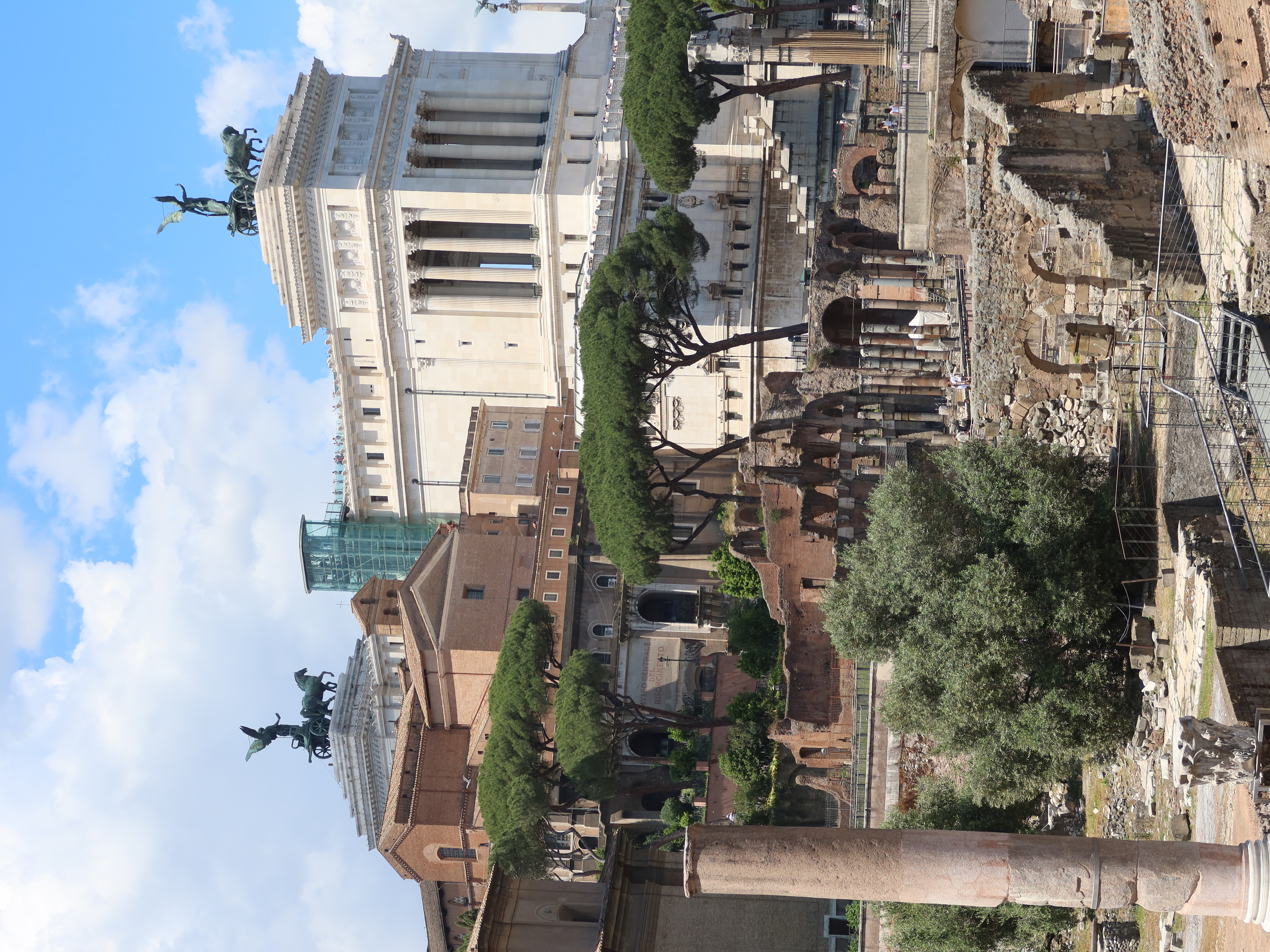 Altar of the Fatherland in Rome, Italy, with ruins, trees, columns, and horse statues, cloudy sky.