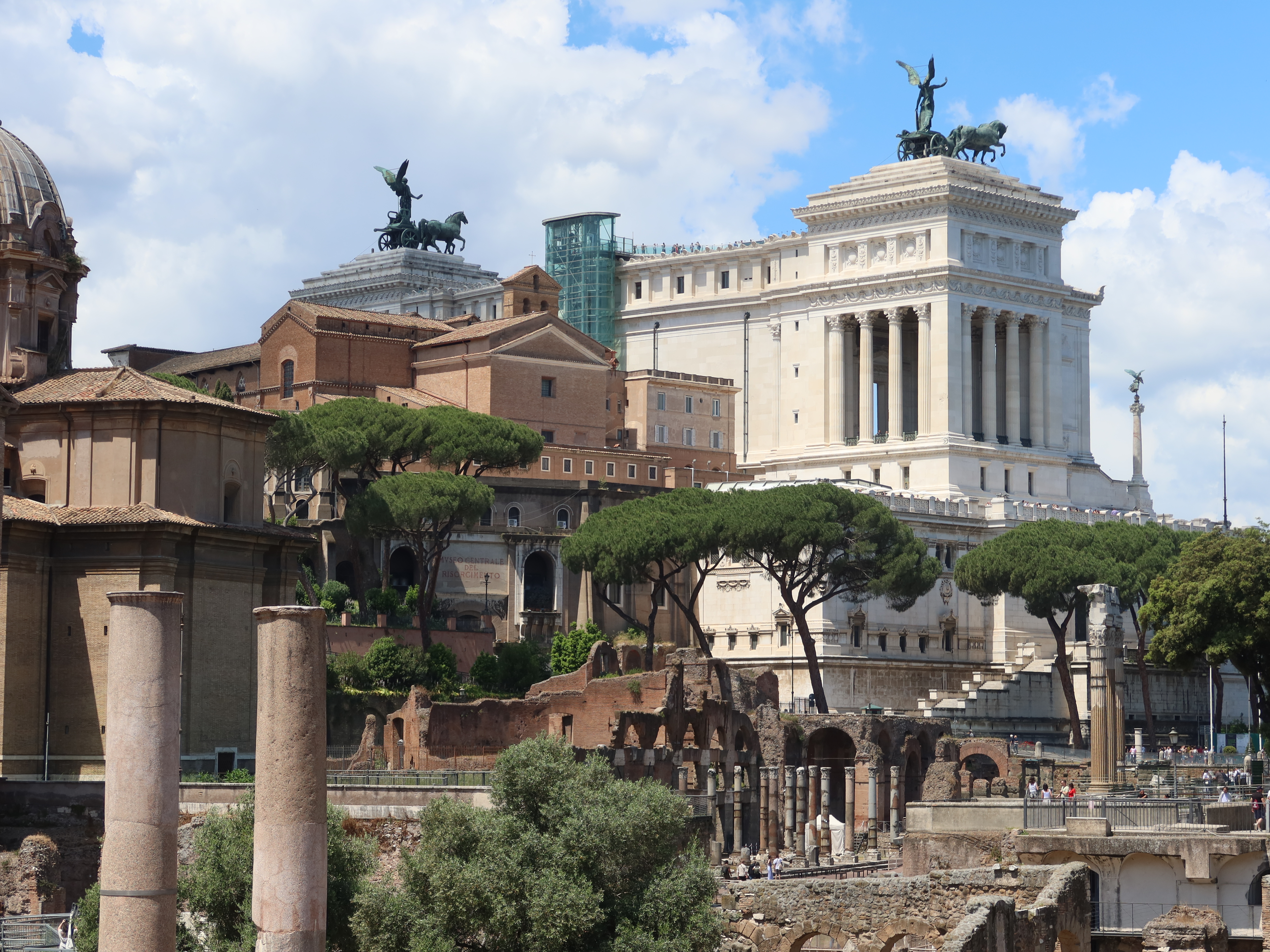 Historic architecture view featuring Altare della Patria, columns, ruins, and pine trees.